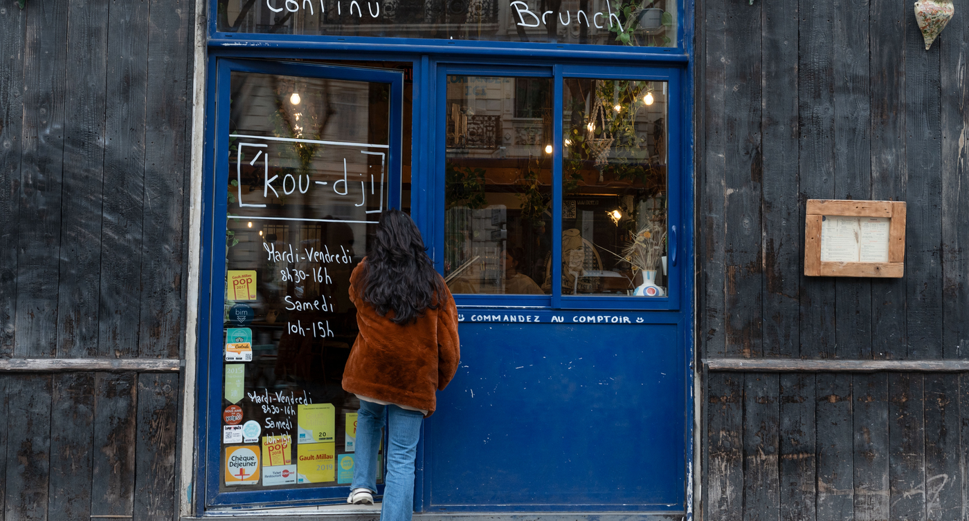 Eine Person steht vor dem Café Coogee in Marseille, betrachtet die Kreidetafel mit den Öffnungszeiten und dem Angebot für kontinuierlichen Service, Frühstück, Mittagessen und Brunch.