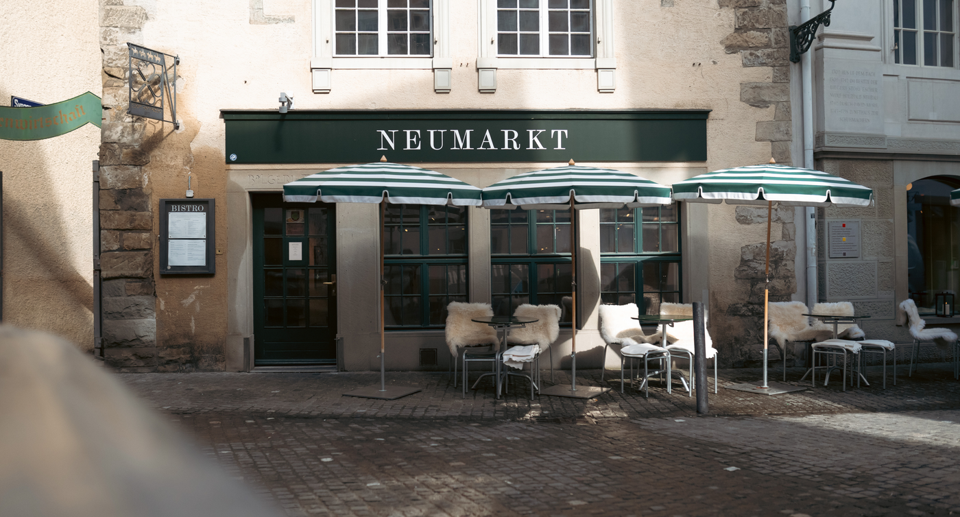Un ristorante con la scritta Neumarkt ha una veranda con posti a sedere e ombrelloni.  