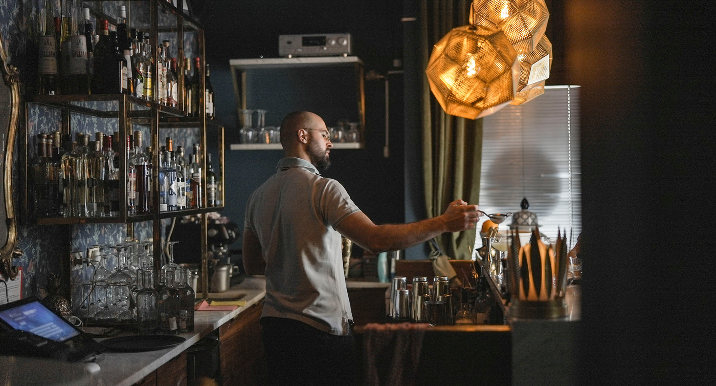 Dietro il bancone, il barman filtra il succo con un colino e lo versa nel bicchiere da cocktail.