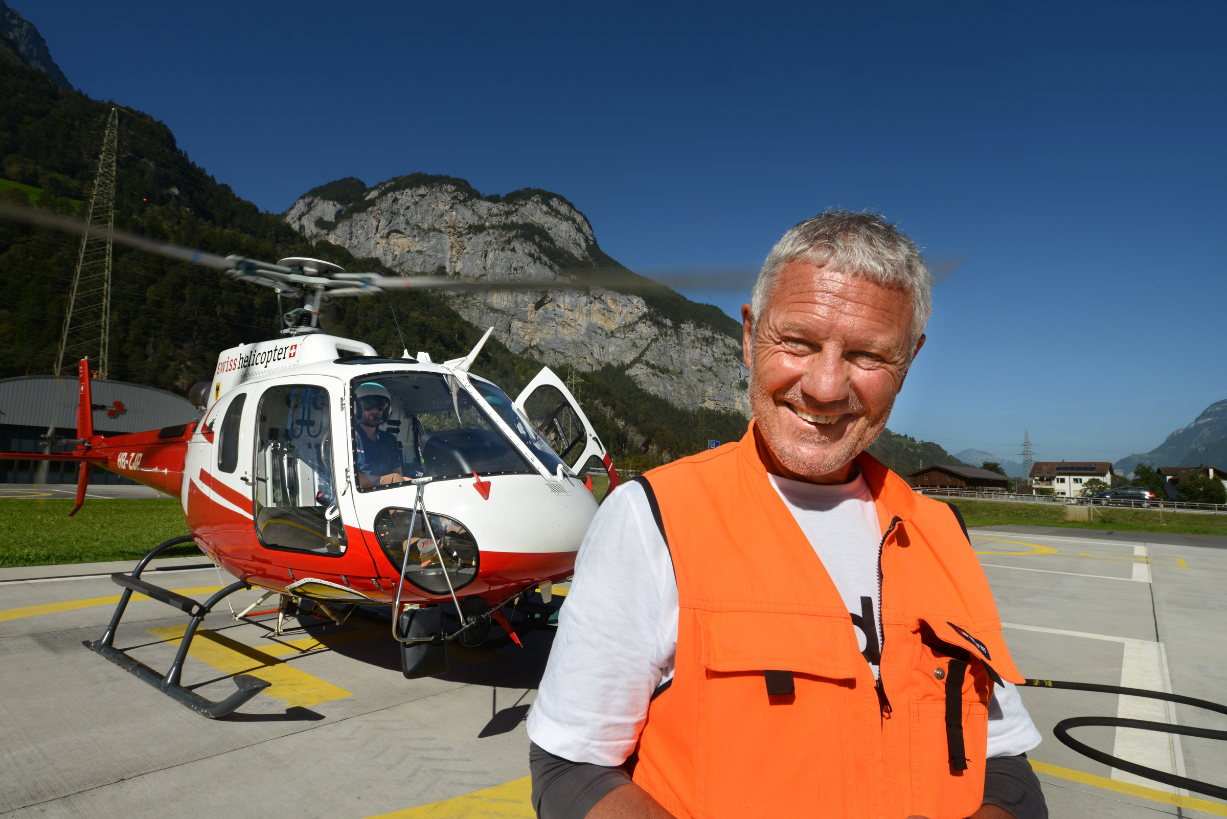 Marc Hauser steht vor einem Helikopter und lächelt in die Kamera. 