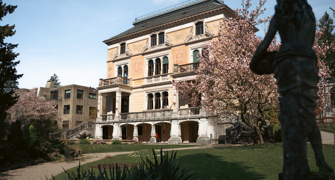 Eine Villa im historistischen Stil ist umgeben von einem grünen Park mit blühenden Blumen.  