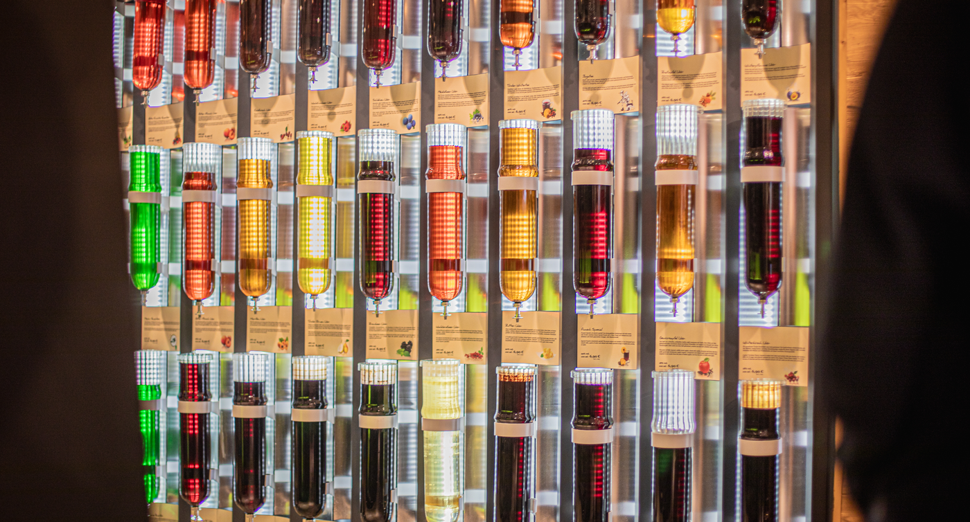 Una parete piena di bottiglie colorate di vetro con liquori e grappe.