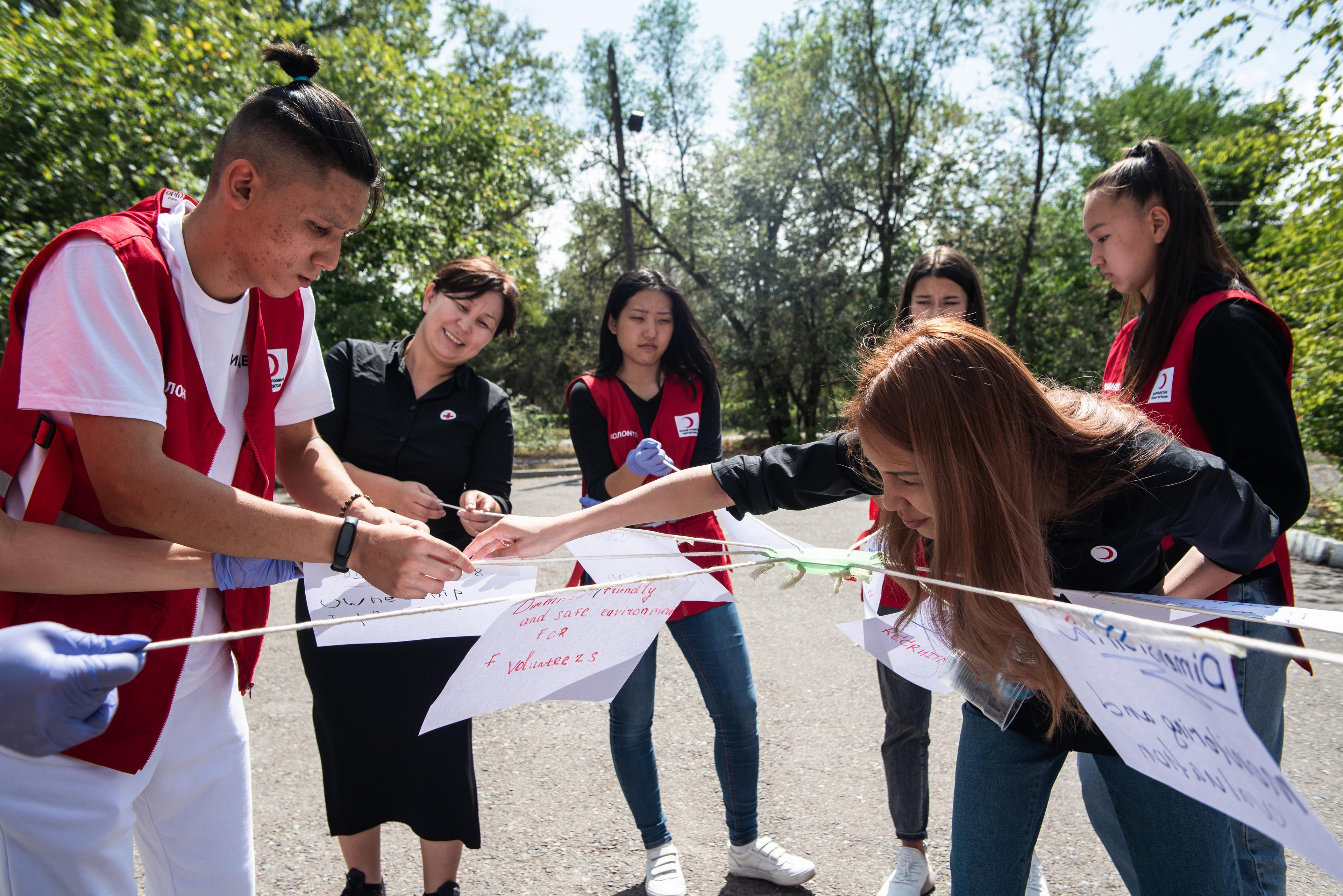 Ein Training mit Freiwilligen des Kirgisischen Roten Halbmondes. Es wurden Schnüre zusammengebunden, wovon jeder ein Ende in der Hand hält. Daran festgemacht sind aufgeschriebene Erkenntnisse und Wünsche.