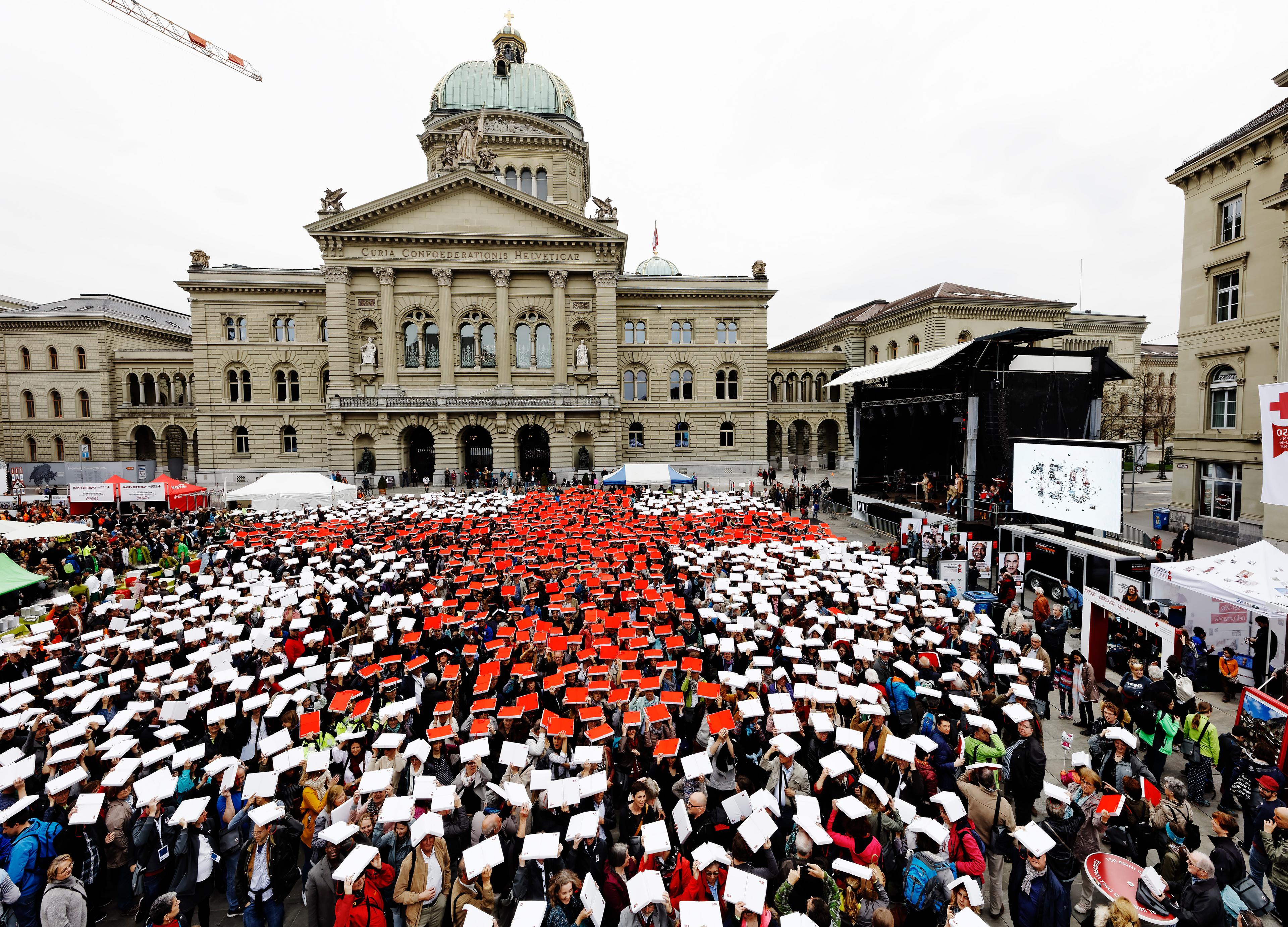 Alcune migliaia di persone formano una grande Croce Rossa su uno sfondo bianco con foglie rosse e bianche nella Bundesplatz di Berna.