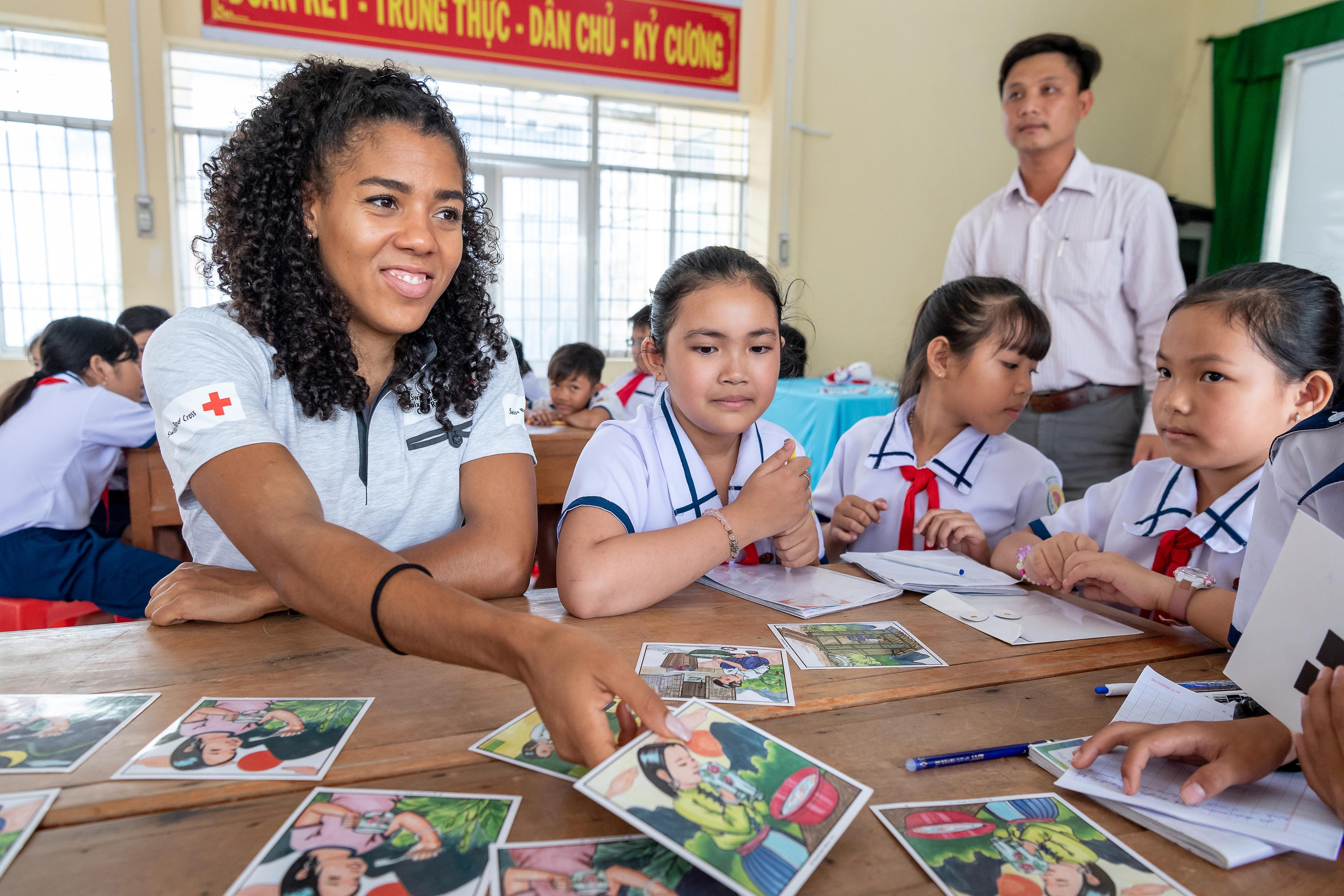 Mujinga Kambundji, sitzt mit Schülerinnen der Schule in Khan Binh Tay an einem Tisch und schaut sich mit ihnen Karten an.