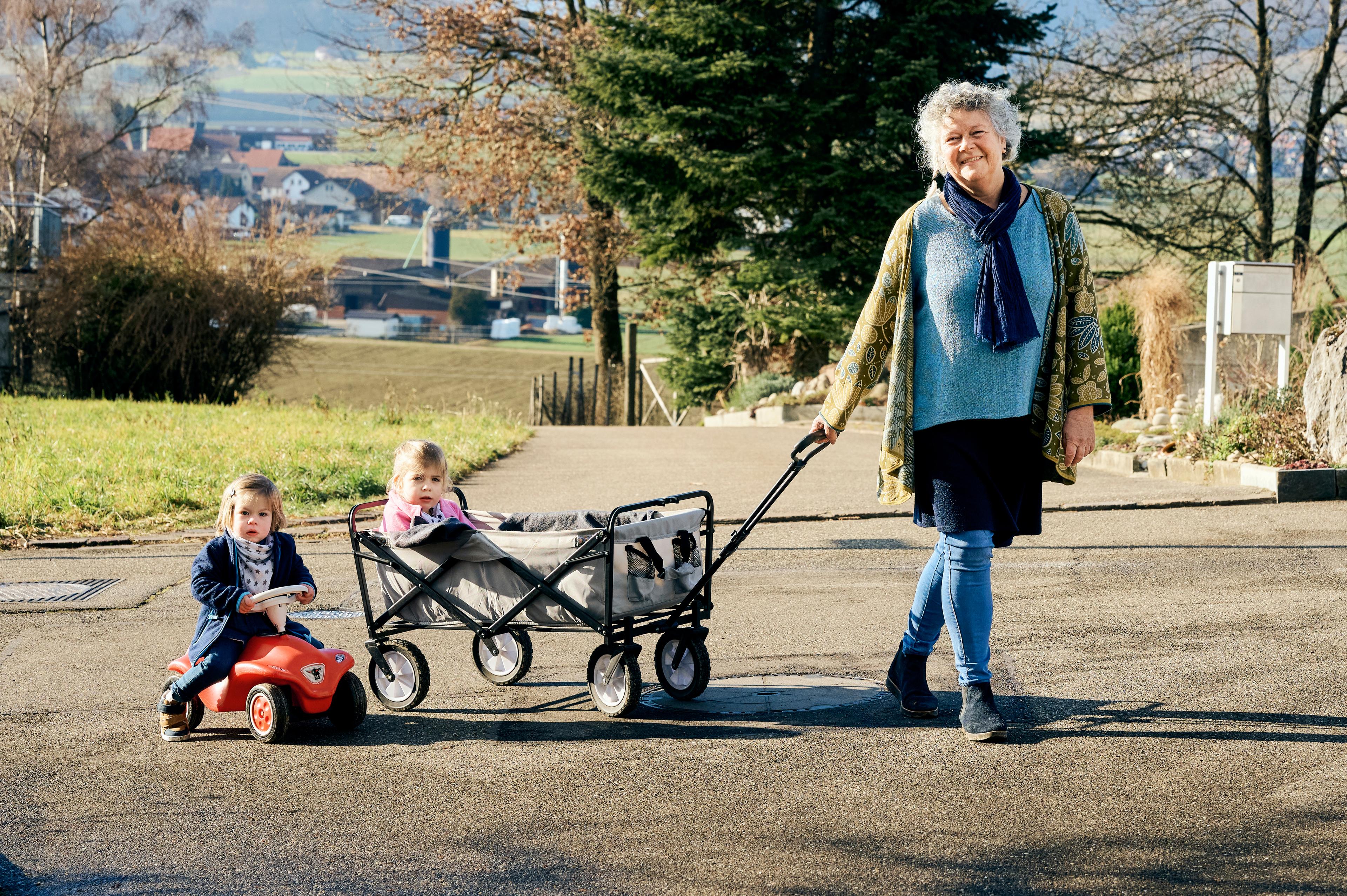 Die Kinderbetreuerin spaziert mit zwei Kindern (Junge und Mädchen. Sie haben einen Leiterwagen dabei