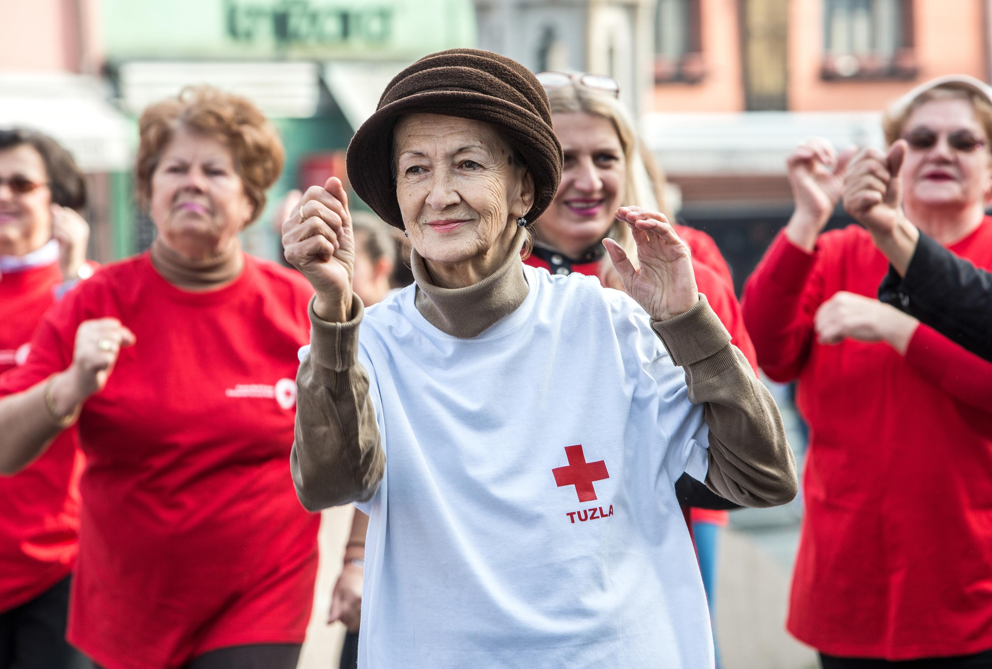 Betagte Frauen beim Bewegungstraining. Sie scheinen am Sport zu erfreuen. Eine ältere Dame trägt einen Hut und ein T-Shirt mit dem Roten Kreuz Tuzla (Bosnien).