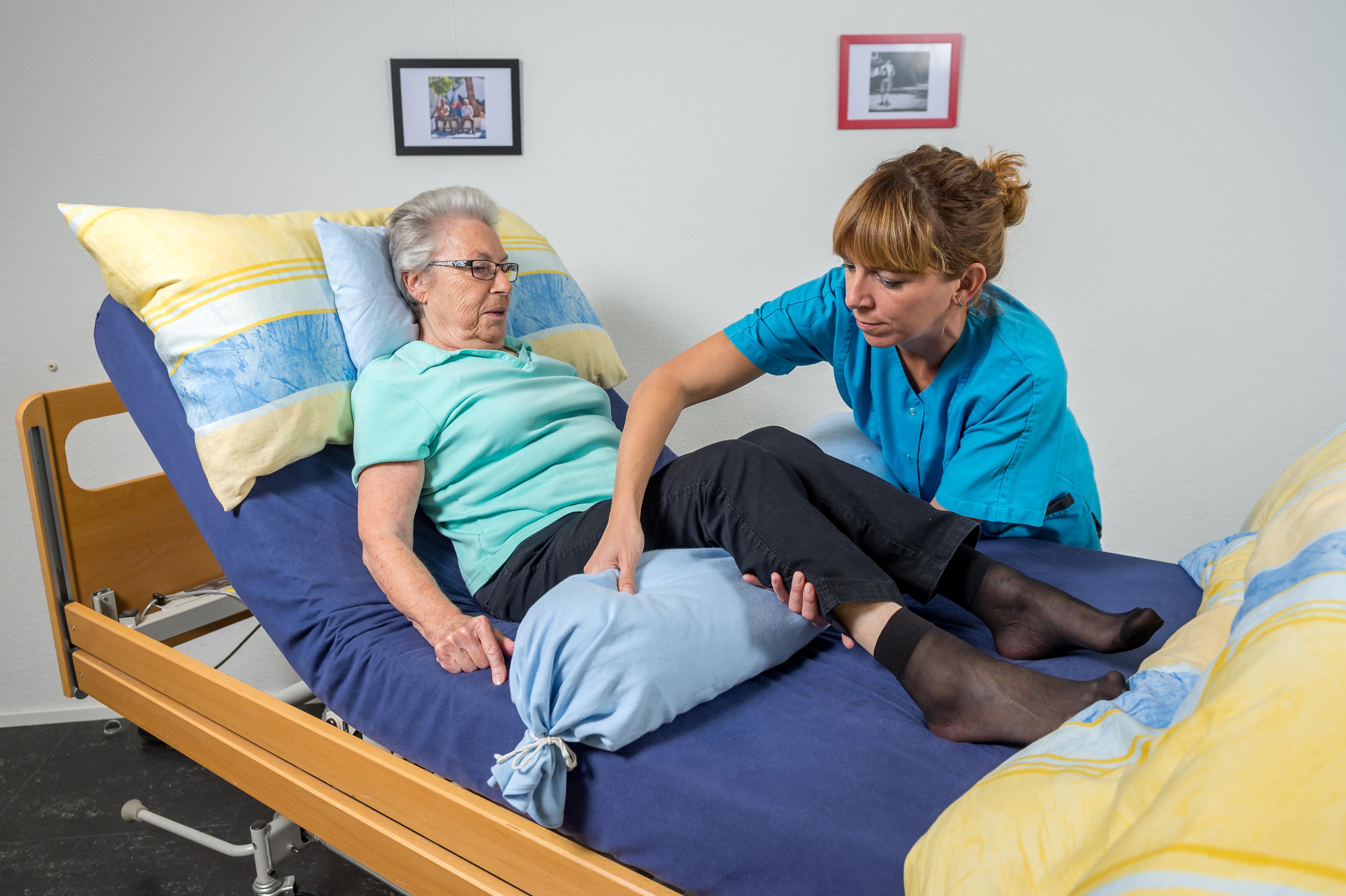 Une aide-soignante redresse les jambes d'une patiente allongée sur le lit pour lui placer les genoux. 