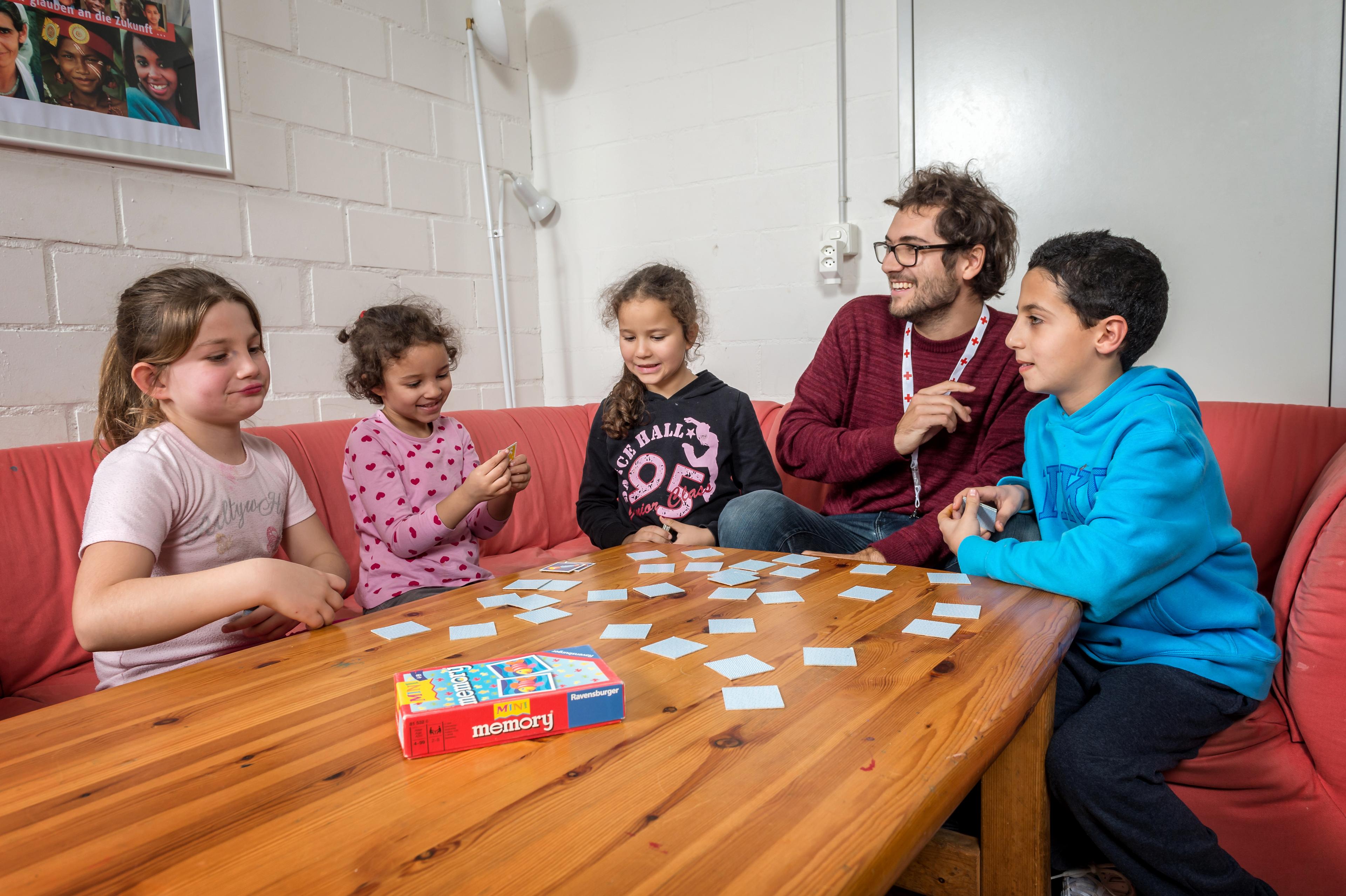 Un giovane volontario della CRS è seduto a un tavolo con quattro bambini. Insieme giocano a carte. 