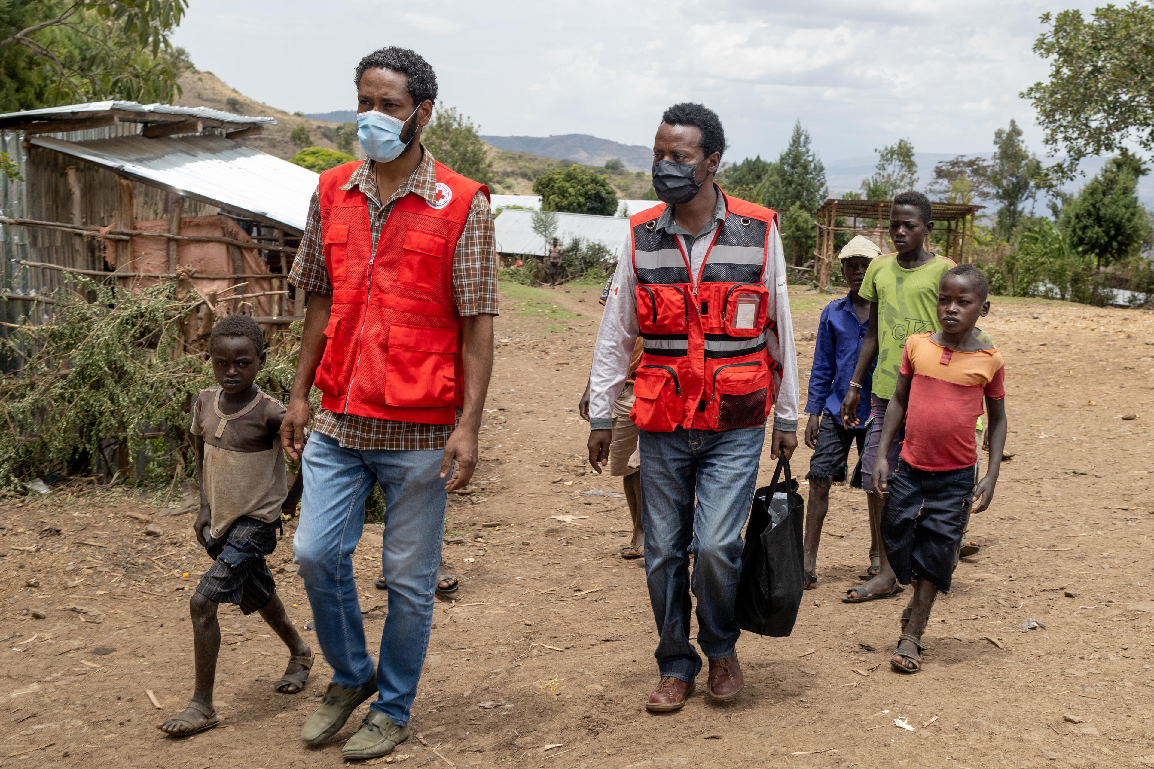 Trois hommes et quatre garçons traversent le village de Kola en Éthiopie, avec quelques huttes en arrière-plan.