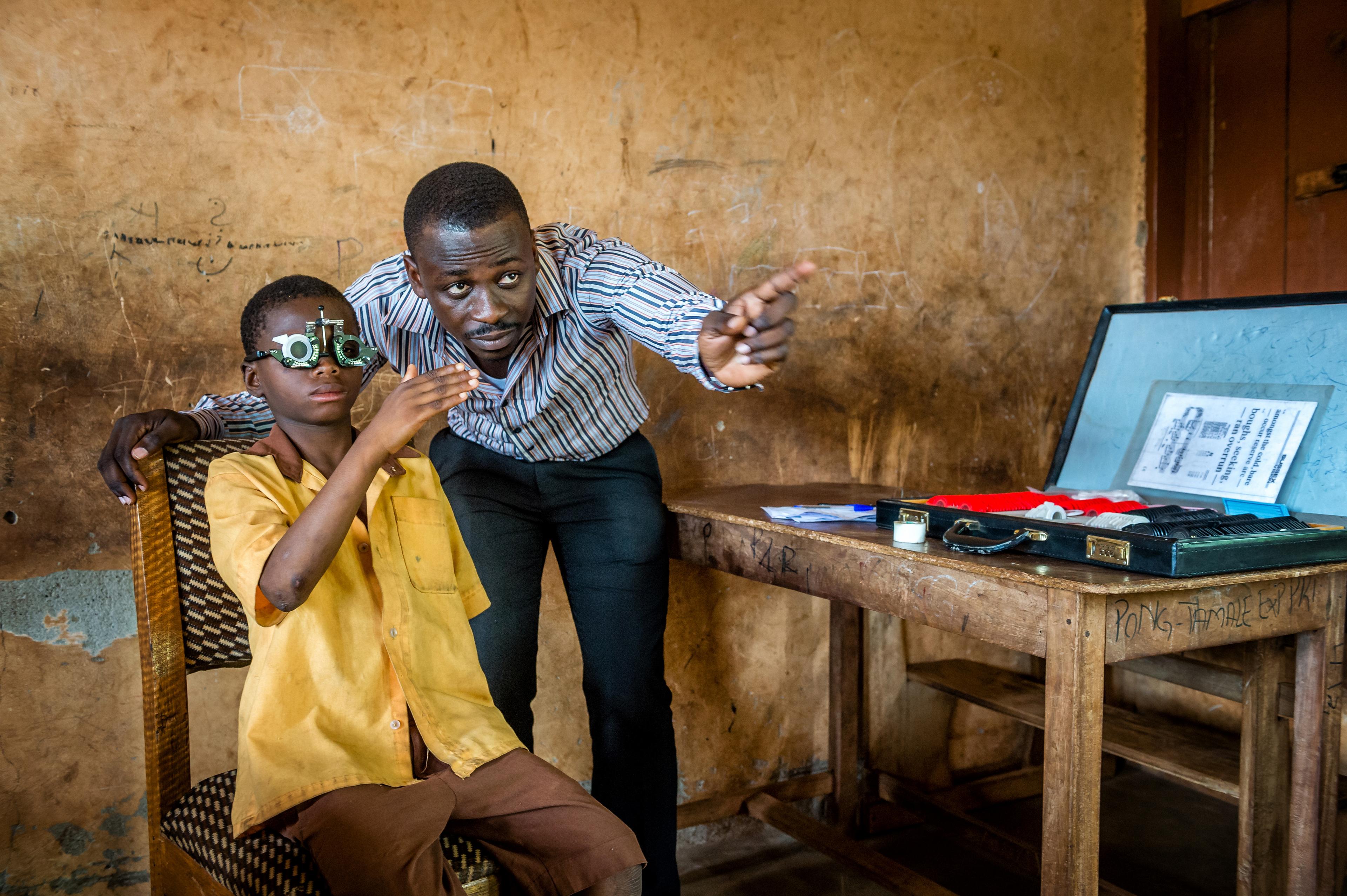 A boy with correction glasses looking forward and one man pointing in the same direction.