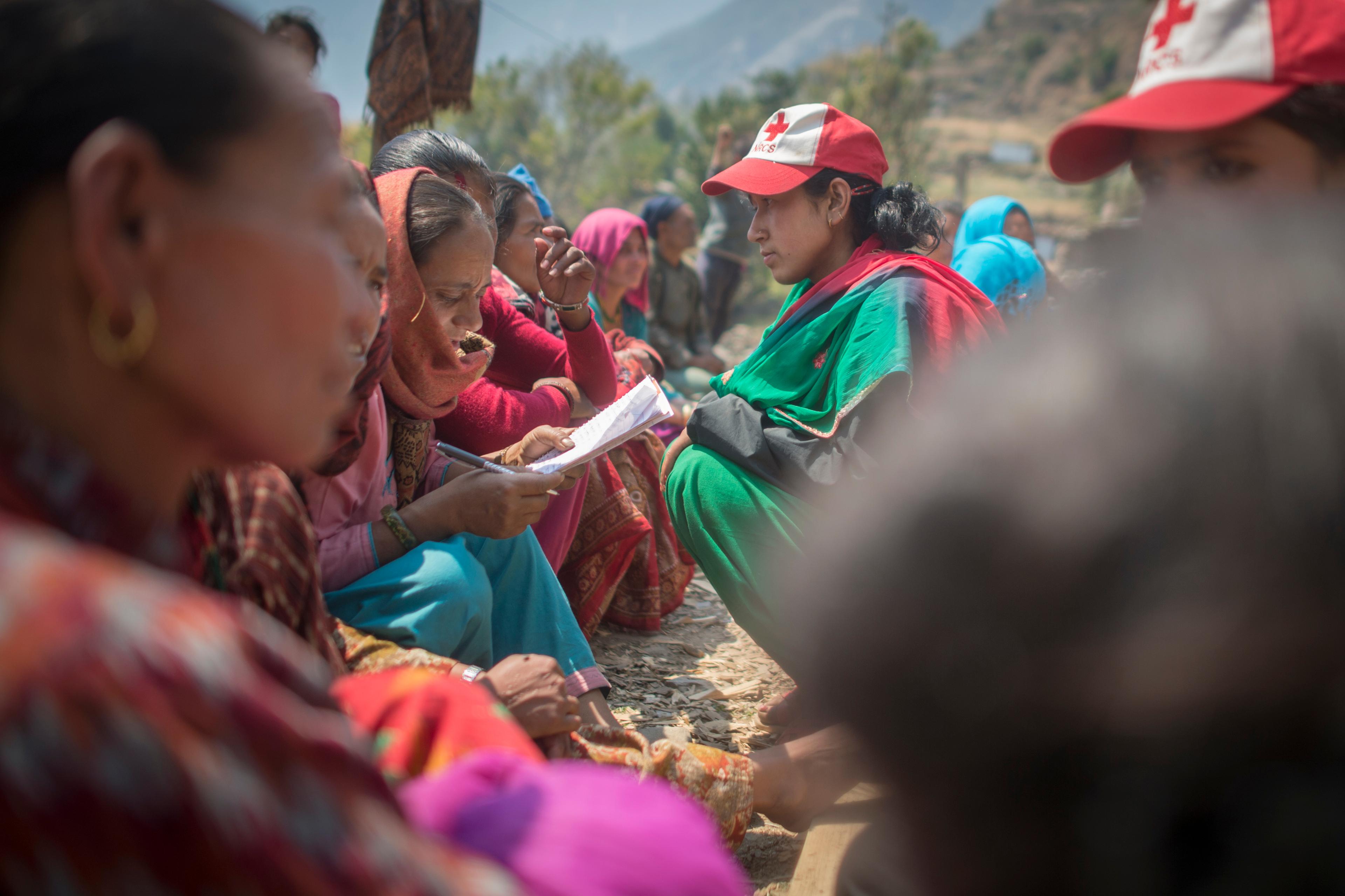 Une bénévole de la Croix-Rouge népalaise s'accroupit devant une participante assise par terre lors d'une formation PASSA à Lapilang, au Népal. Celle-ci remplit un formulaire.