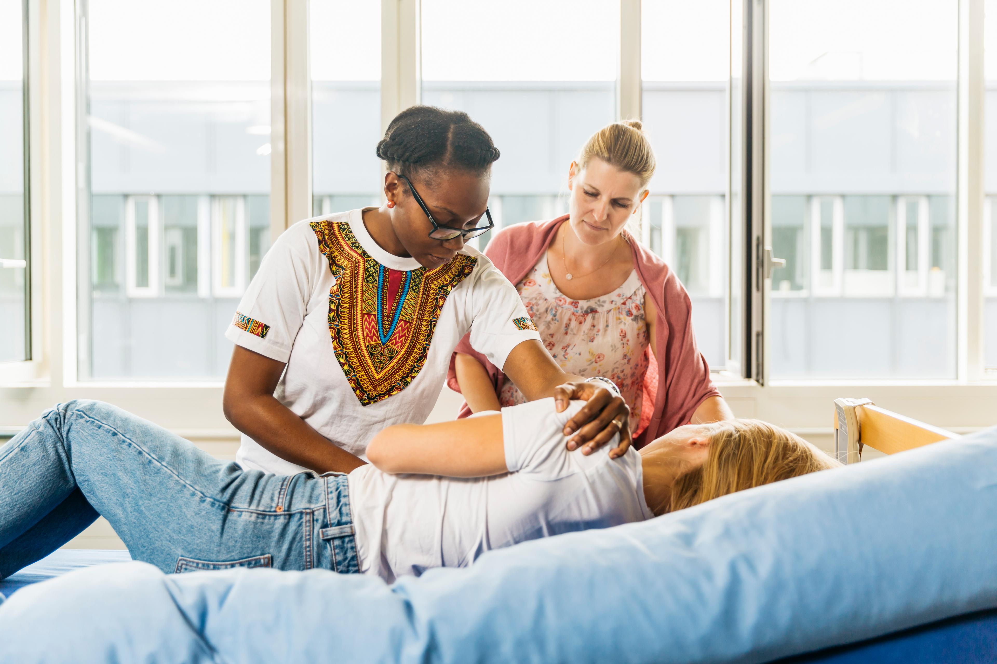 Une aide-soignante en formation s'exerce à positionner une patiente allongée dans son lit.