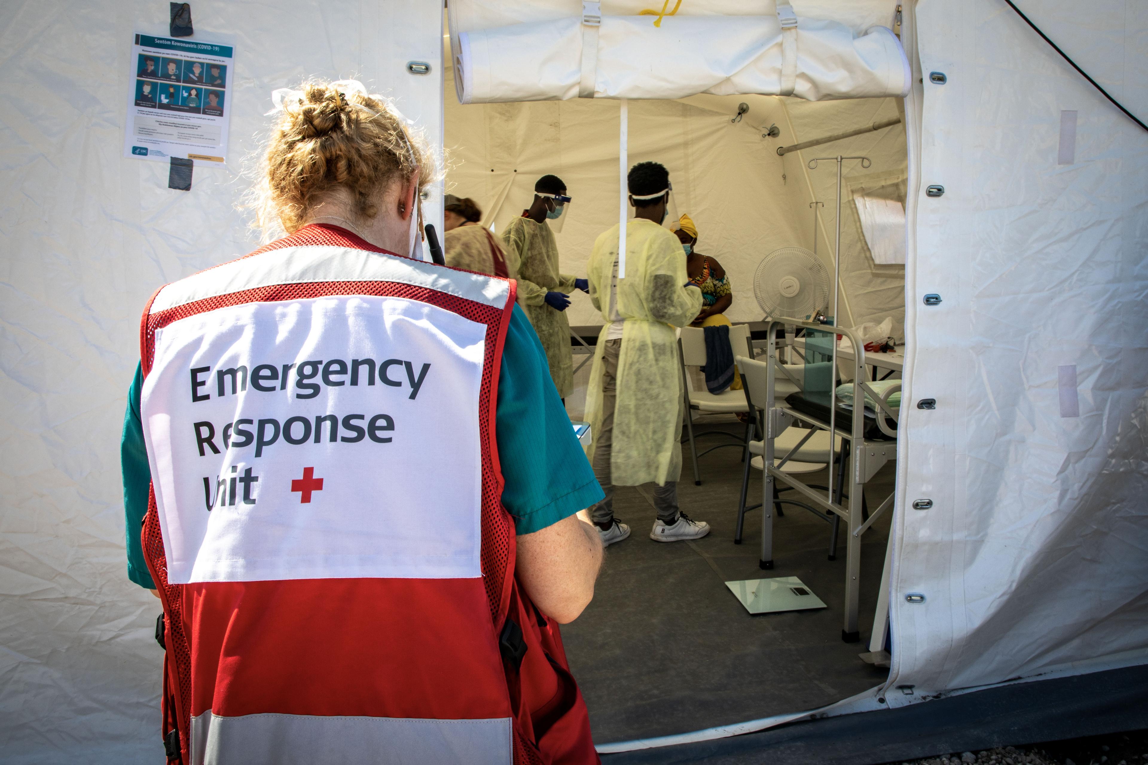A woman from the Emergency Response unit walks towards a tent with a medical team and a patient.