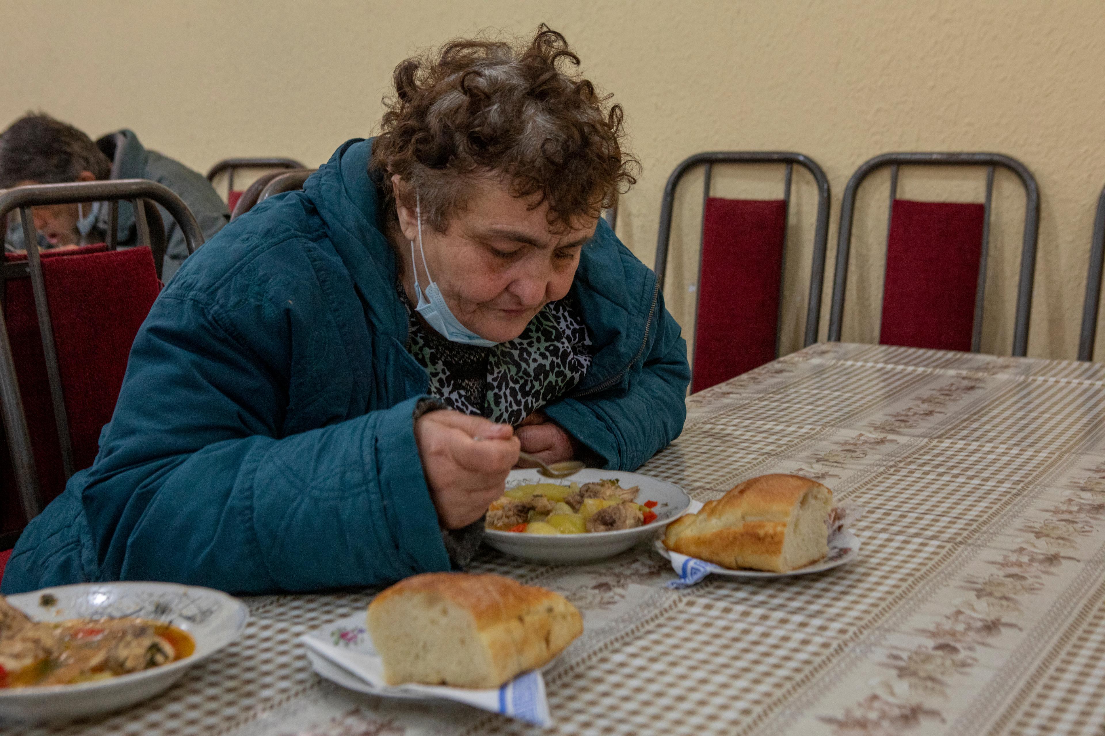 Die Frau sitzt an einem Tisch und isst eine Mahlzeit der Suppenküche.