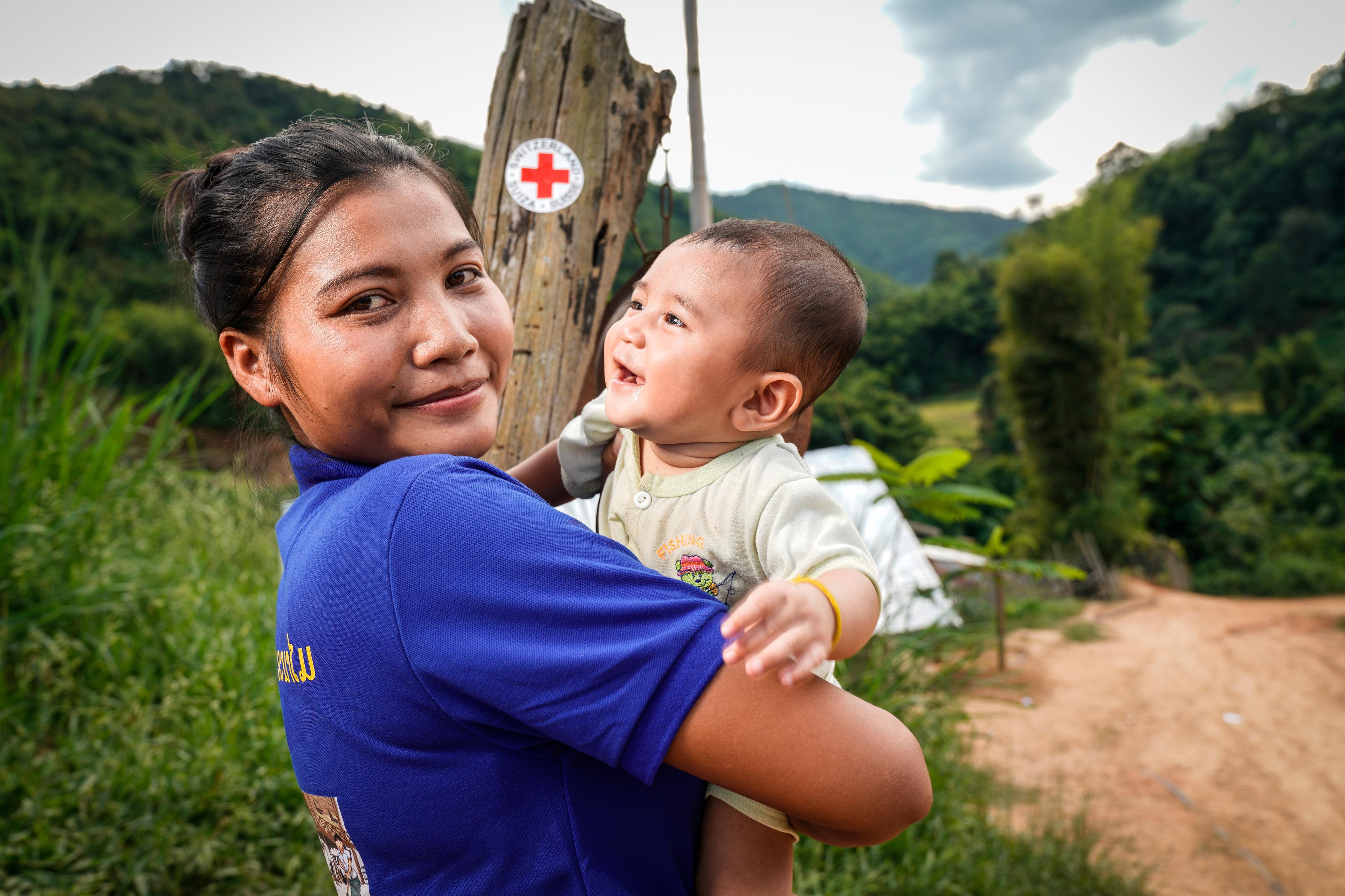 Una volontaria della Croce Rossa con un bambino in braccio che le sorride. Nel distretto di Phonexay, provincia di Luang Prabang, Laos.