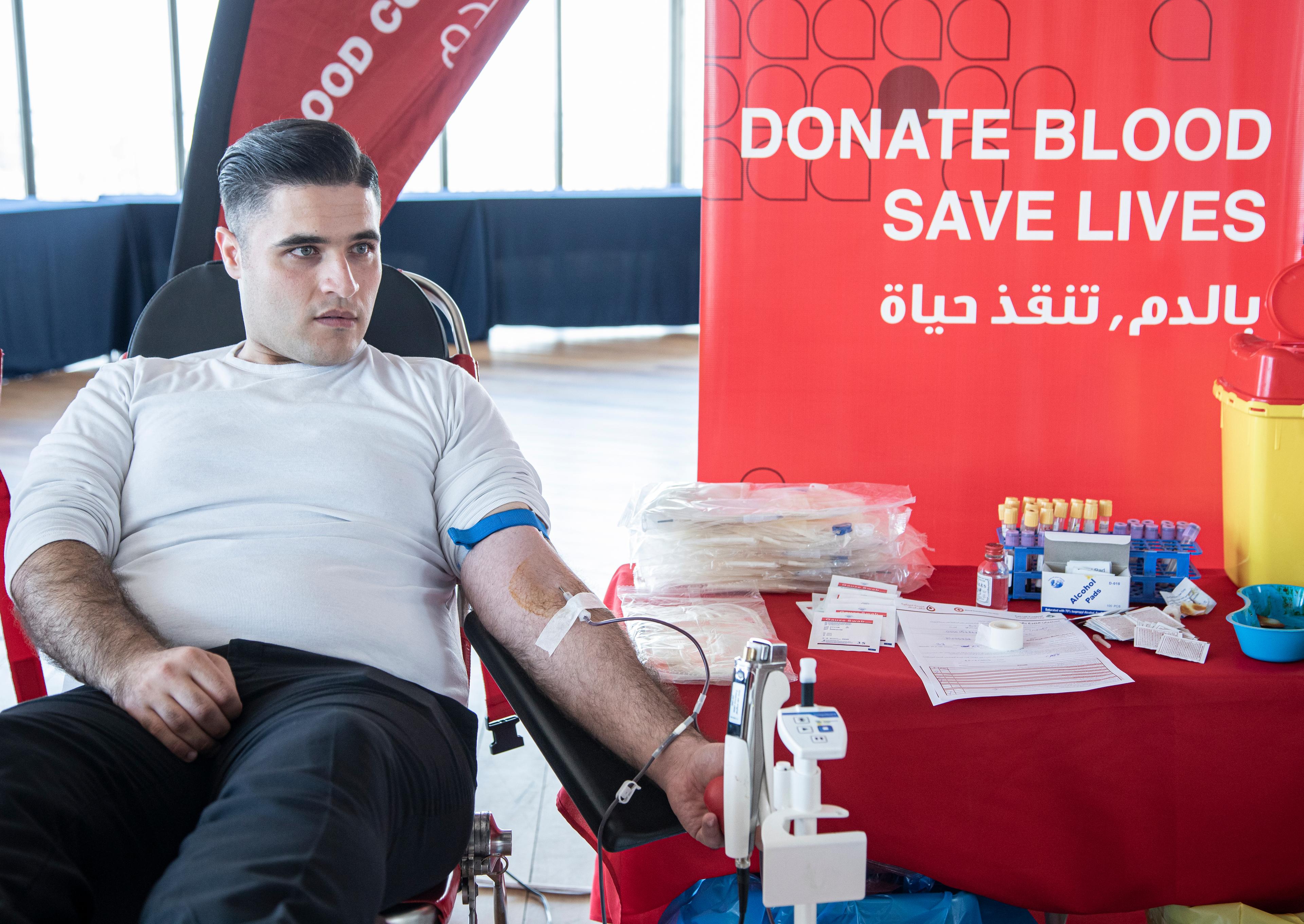 A man donating blood at the Lebanese Red Cross. He is sitting on a chair and has a small tube on his arm.
