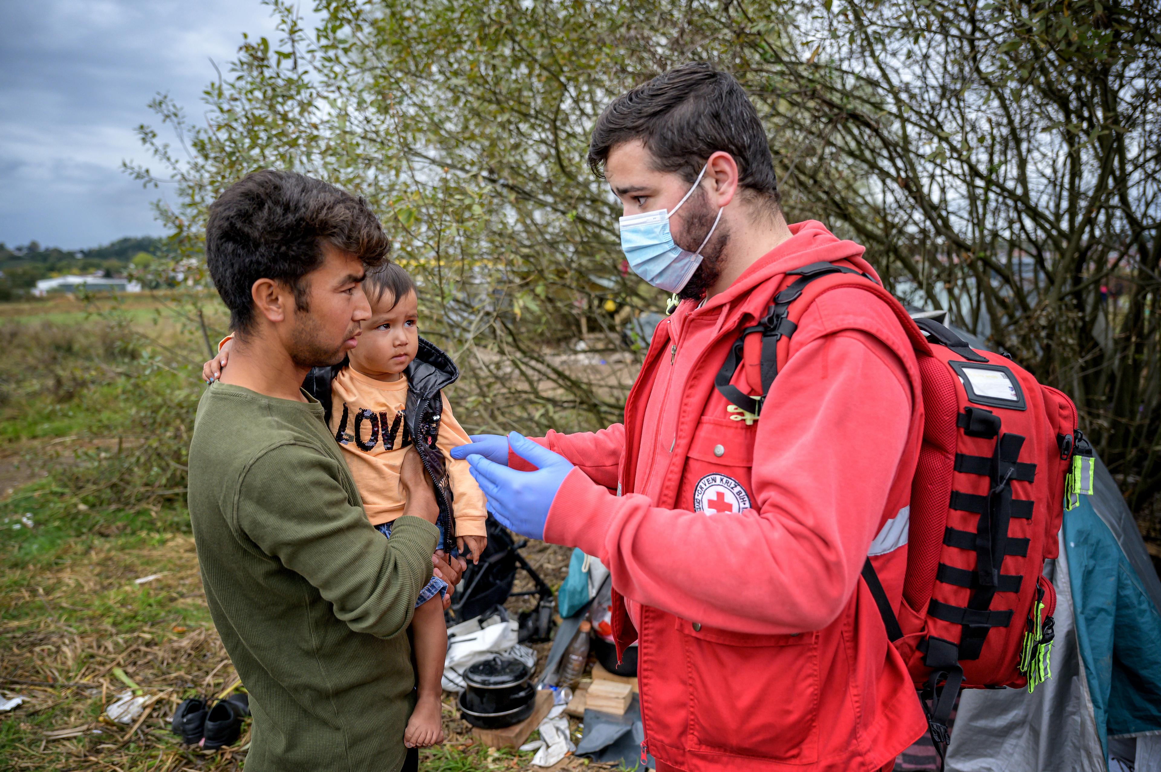 Un homme en uniforme de la Croix-Rouge s'approche d'un père et son enfant. Il semble contrôler l'état de santé de l'enfant.