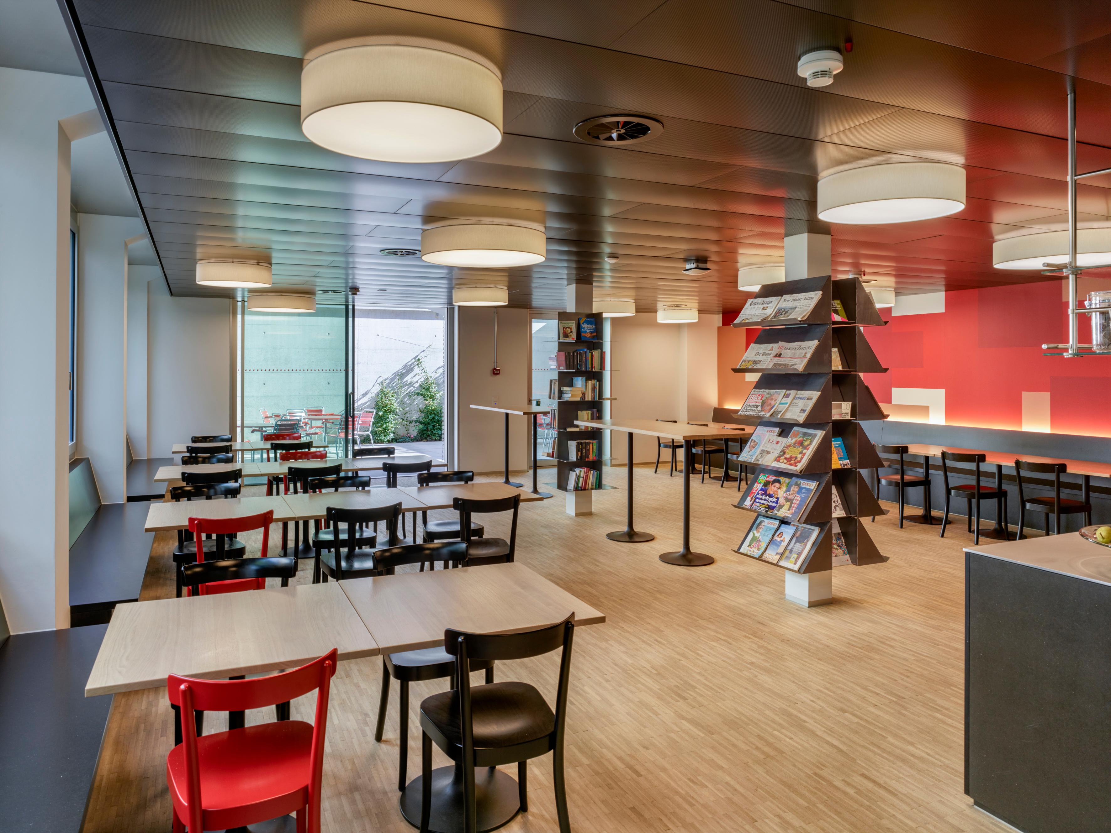 View into the cafeteria of the SRC national office. Chairs, tables, the exit to the small terrace and a shelf with magazines and books.