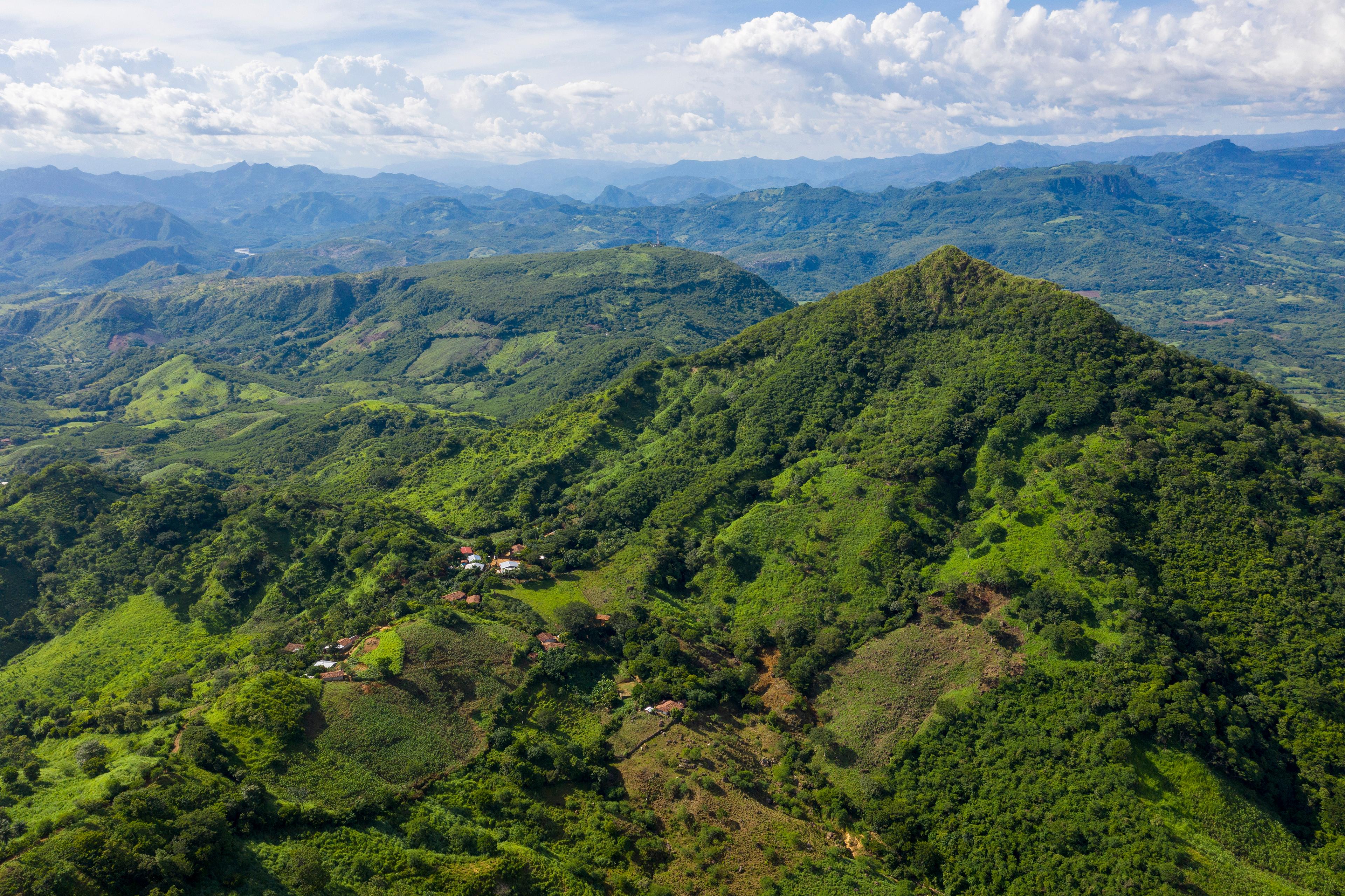 Verdi colline ricoperte di vegetazione si estendono fino all'orizzonte. Nelle valli si trovano alcune case.