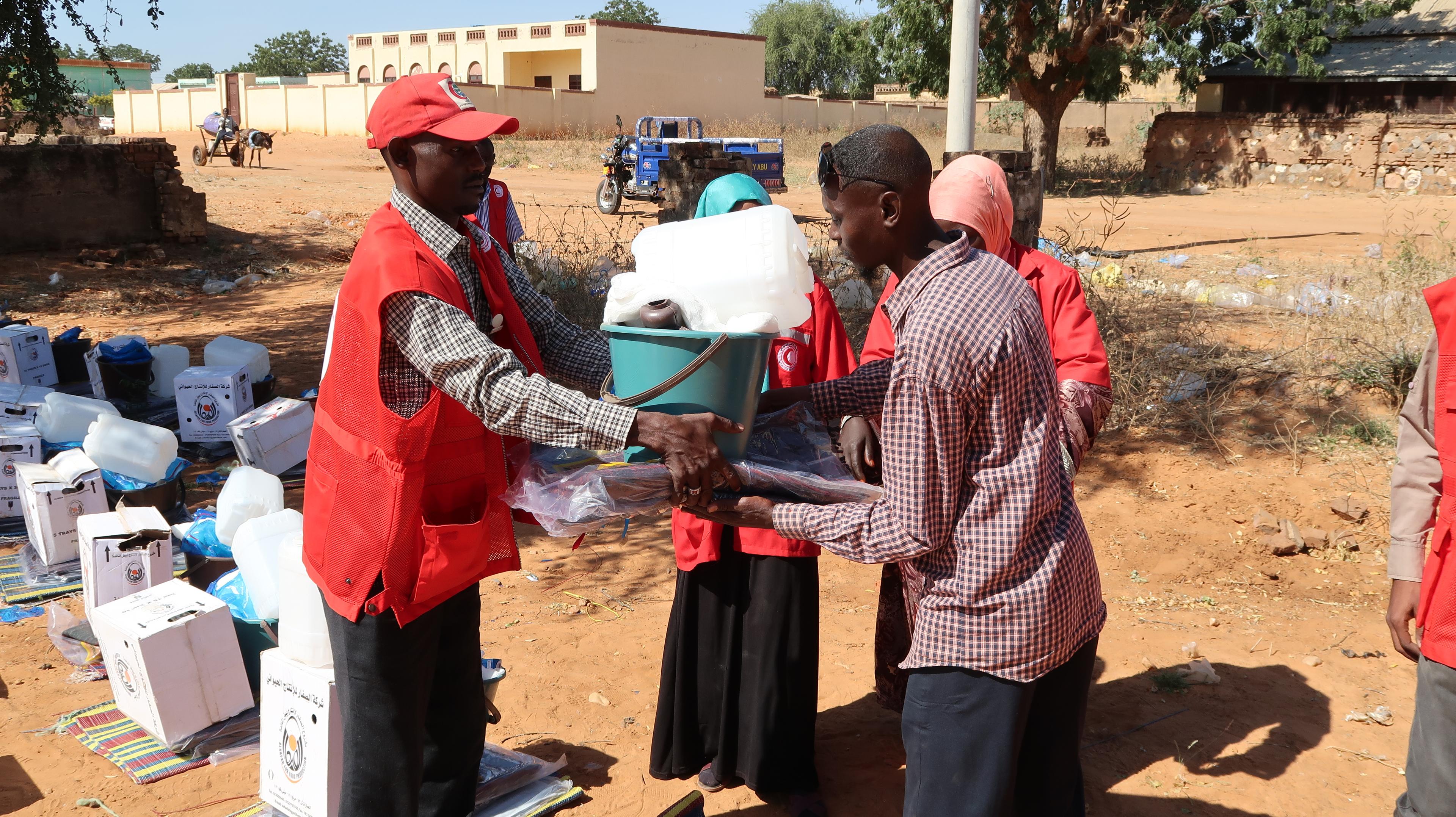 Un uomo in uniforme della Croce Rossa distribuisce beni di prima necessità.