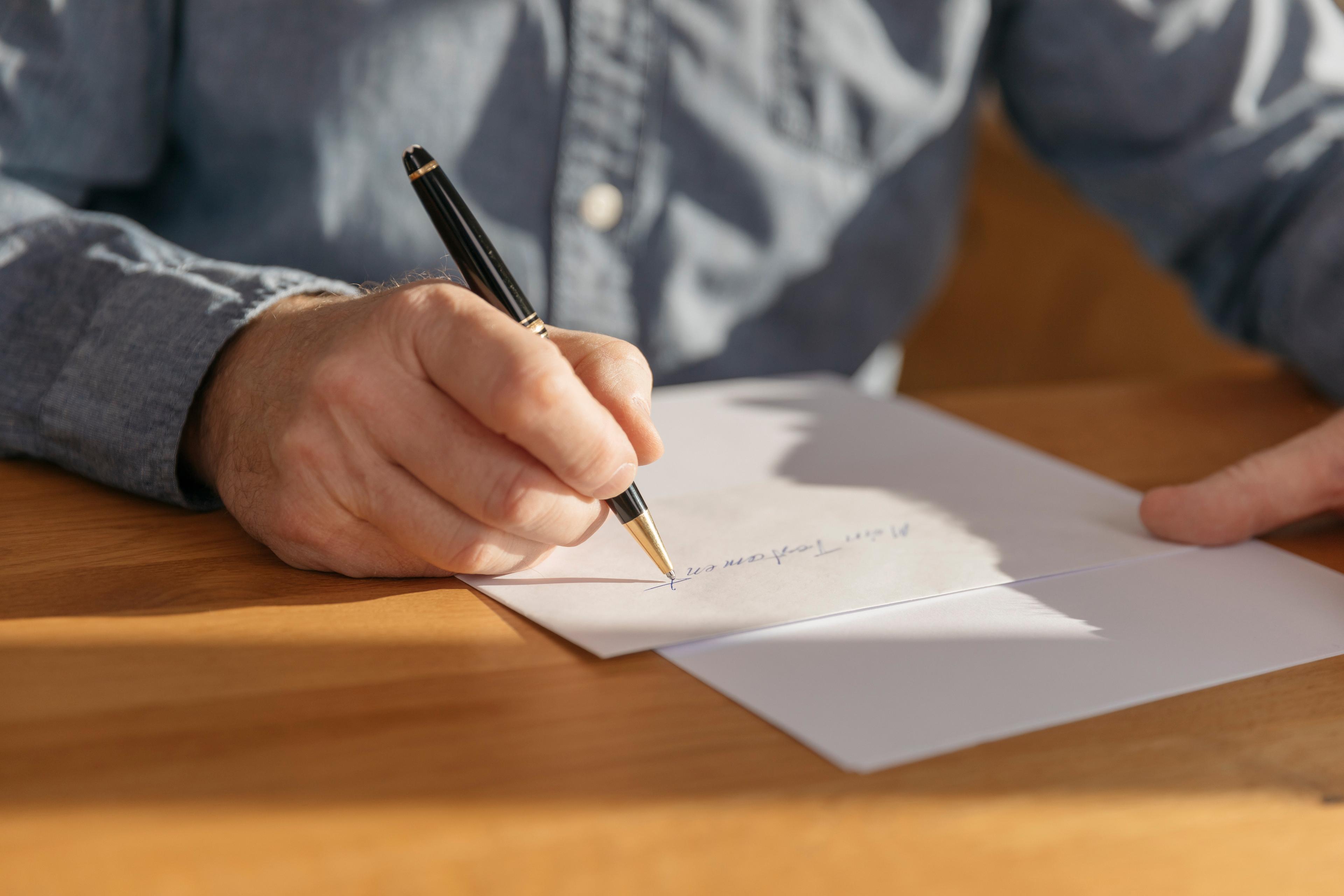 Une main avec un stylo à bille qui écrit "Mon testament" sur une feuille de papier.