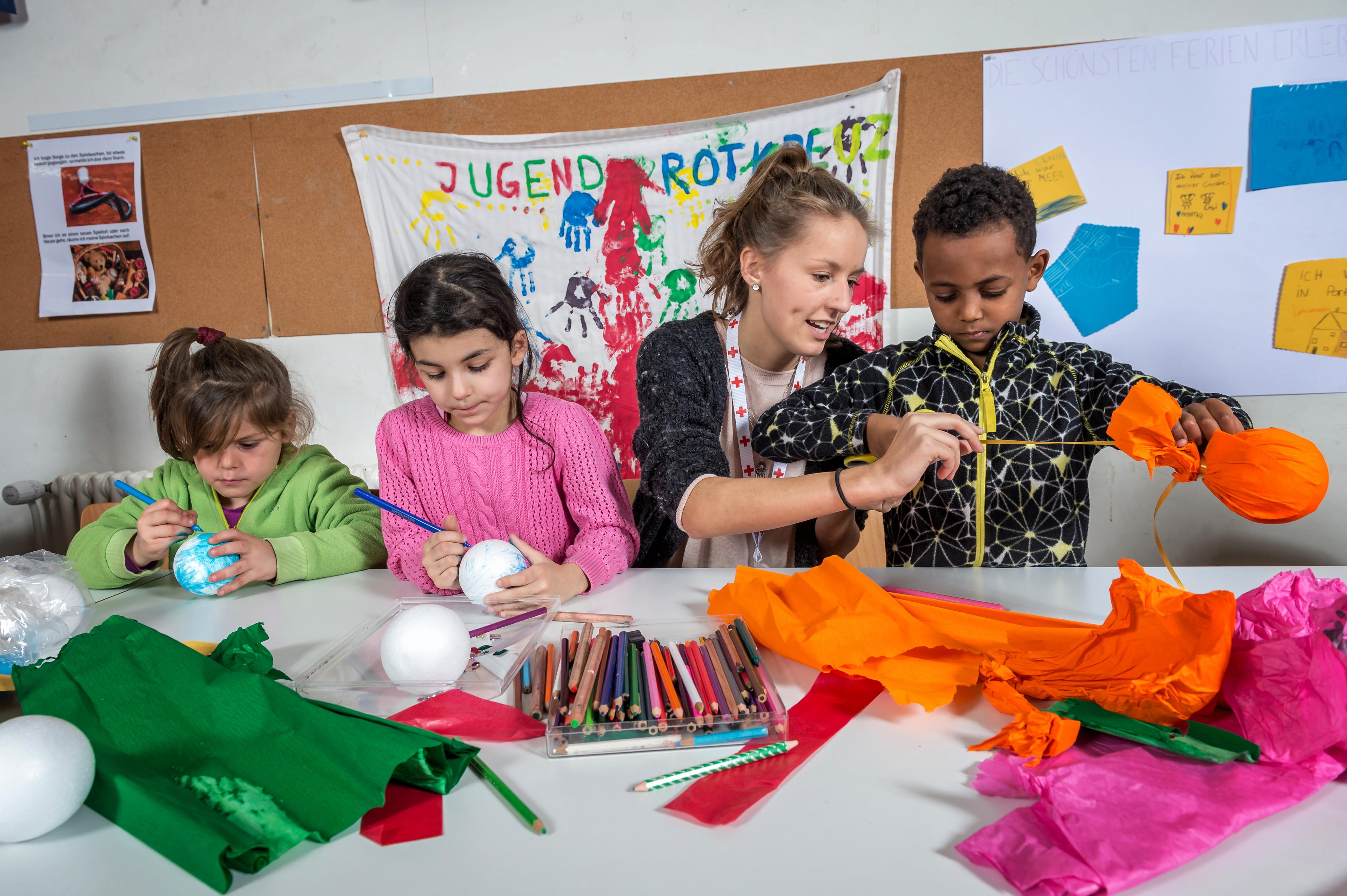 Chiara, 18 anni, della Croce Rossa Giovanile di Basilea, fa lavori di artigianato con tre bambini. Dipingono palline o le avvolgono in carta colorata.