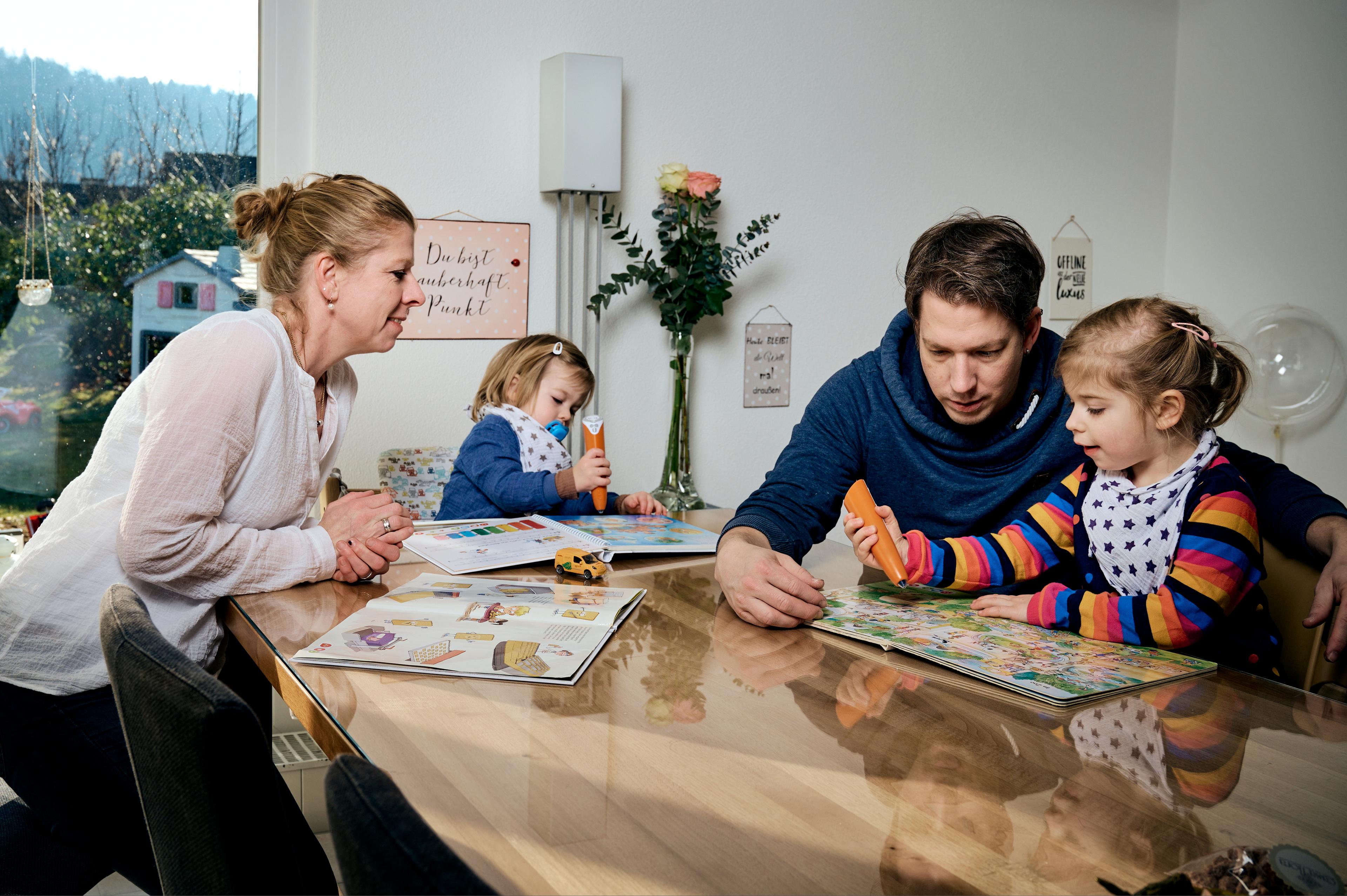 Mutter und Vater mit einem Mädchen (4 Jahre) und einem Jungen (2 Jahre) sitzen am Esstisch und spielen zusammen.