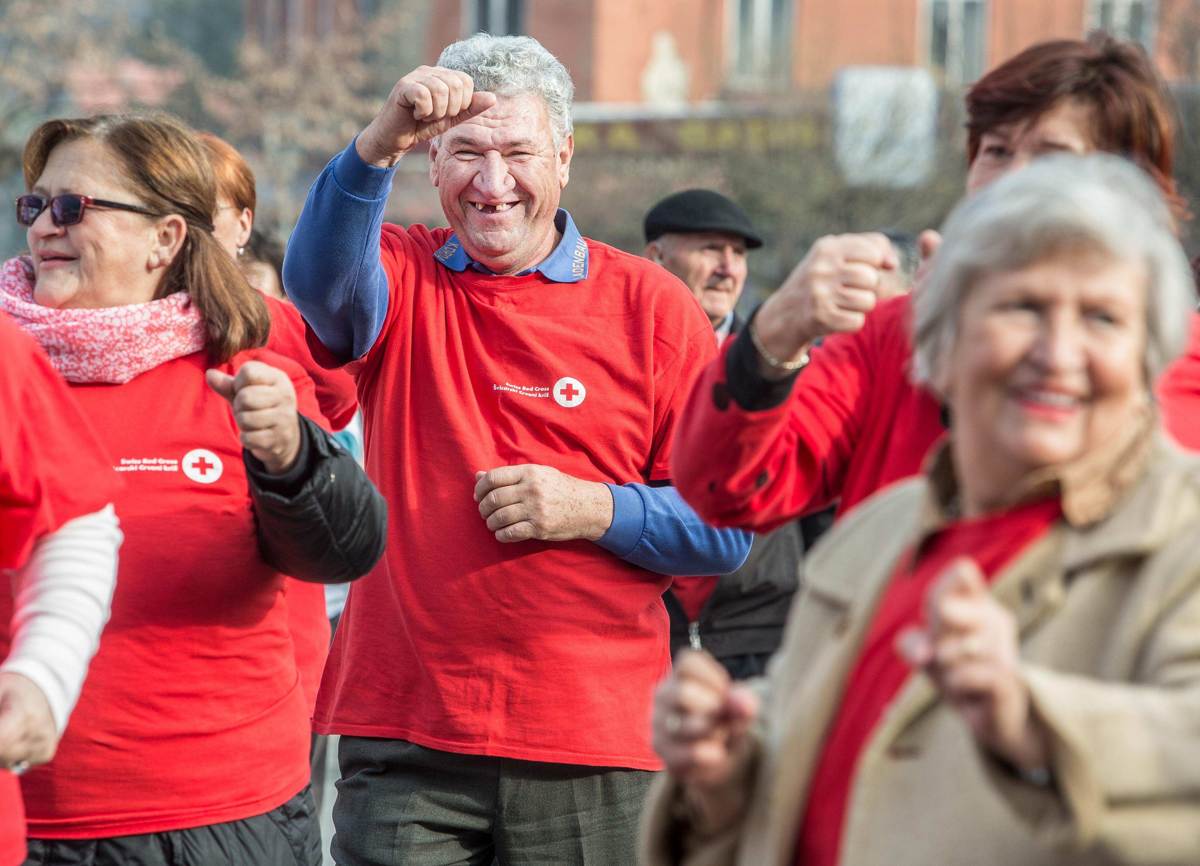 Older people exercising together. They are wearing Red Cross T-shirts and seem to be having fun.