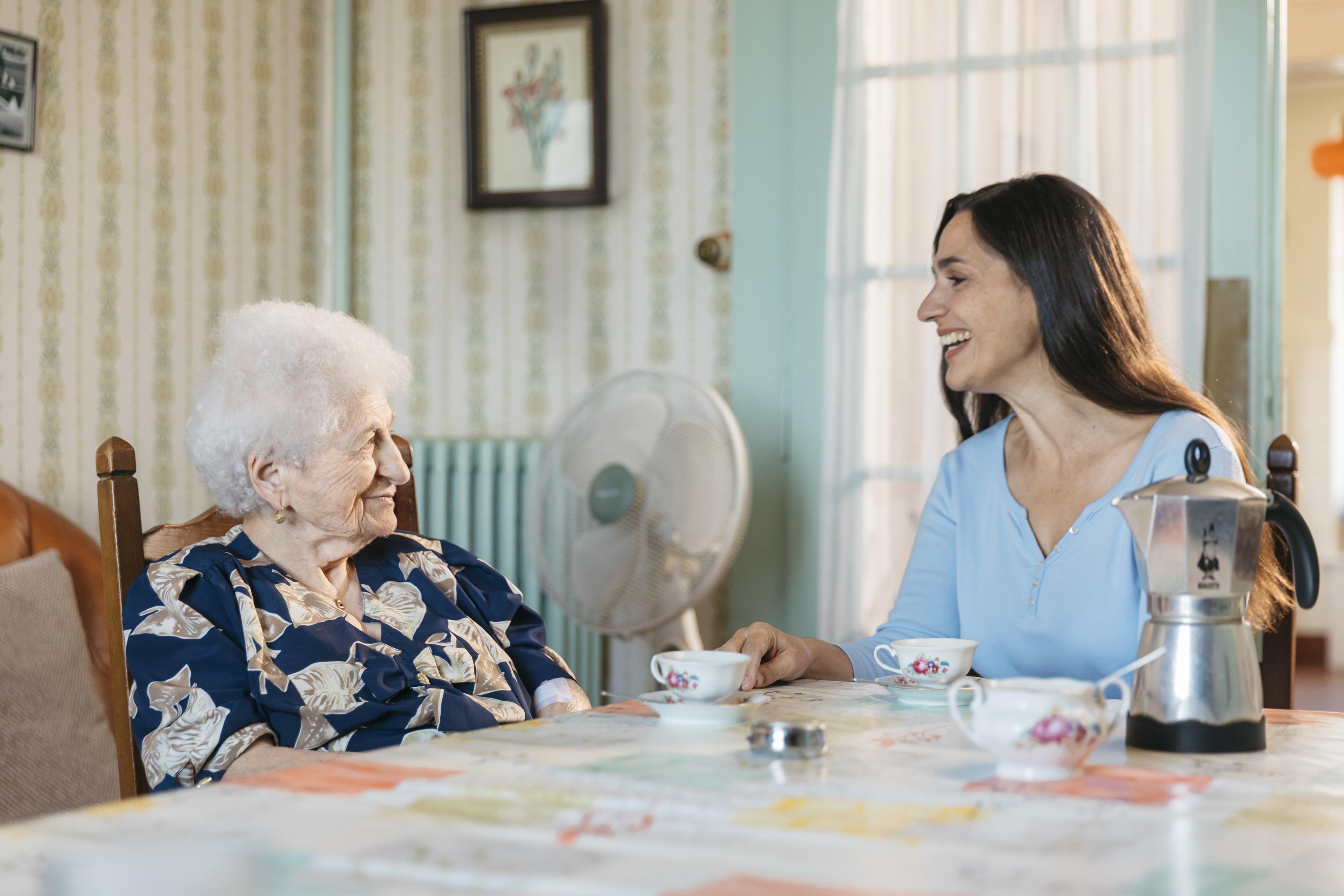 Service de visite et d'accompagnement : une visiteuse bénévole est assise à table avec une femme âgée, une cafetière et deux tasses sont à disposition.