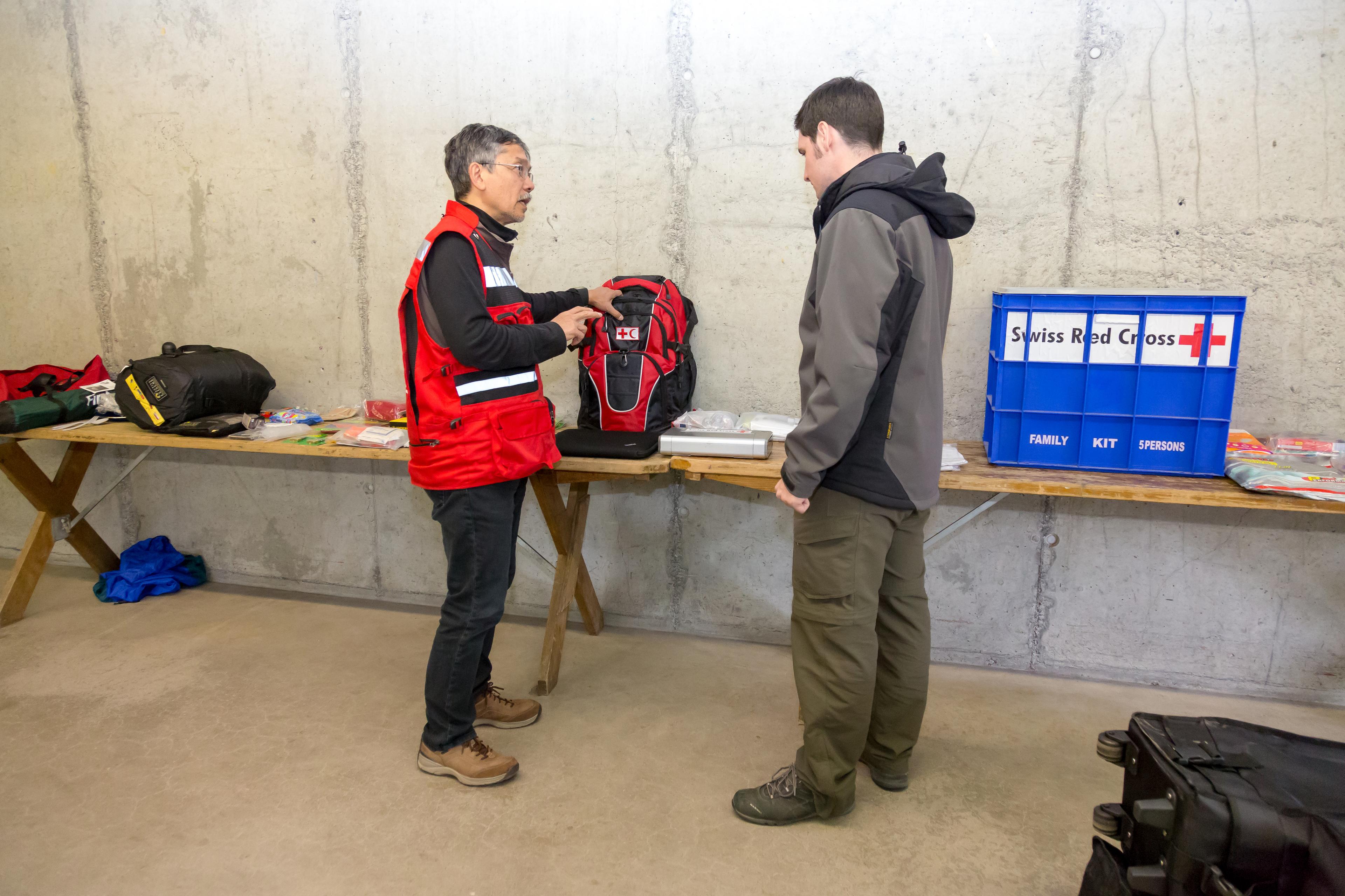 Daniel Garnier, Schweizerisches Rotes Kreuz, erklärt dem zukünftigen ERU-Mitarbeiter Benjamin Bianchi It- und Kommunikationsequipement, welches sich im Rucksack befindet.