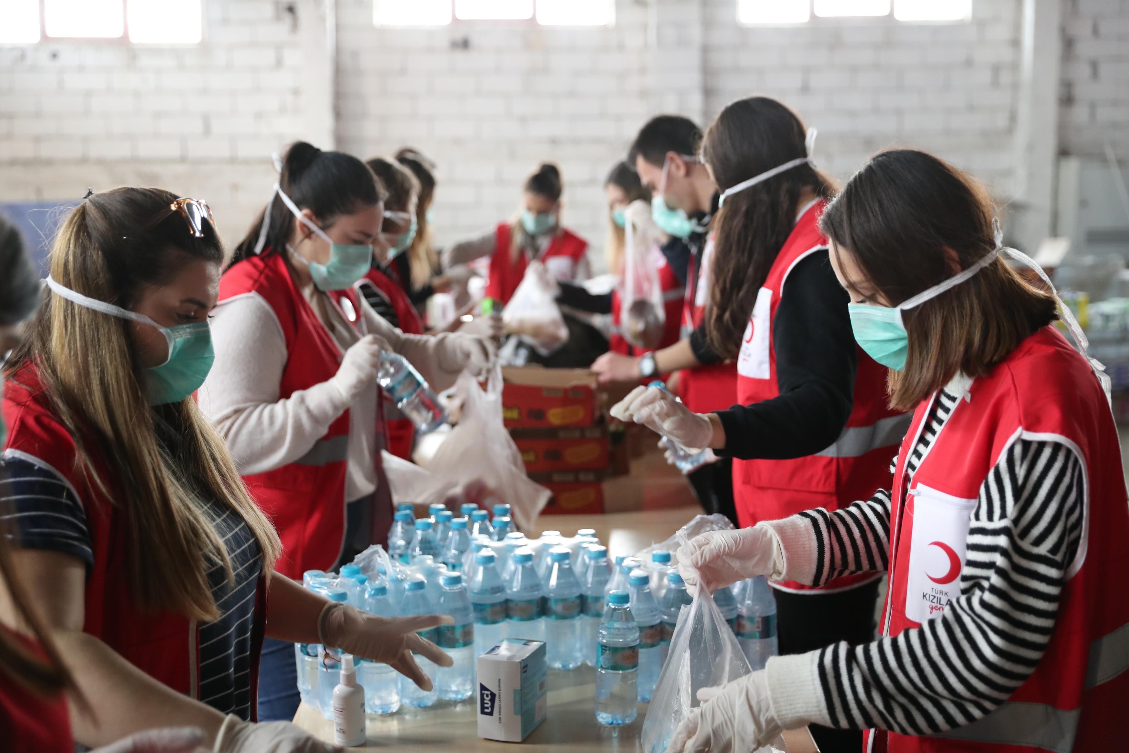 Neuf bénévoles, probablement tous du Croissant-Rouge turc, se tiennent à une longue table et préparent des paquets d'aide.
