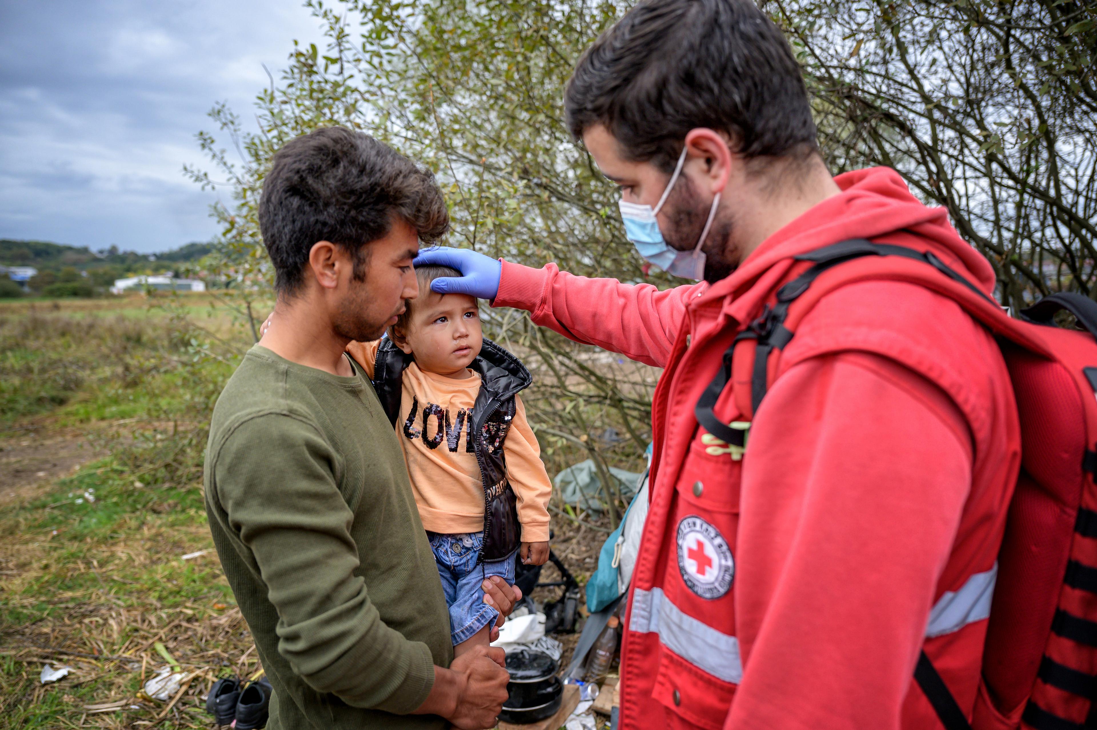 Un volontaire de la Croix-Rouge s'occupe d'un père réfugié et de son enfant en bas âge.