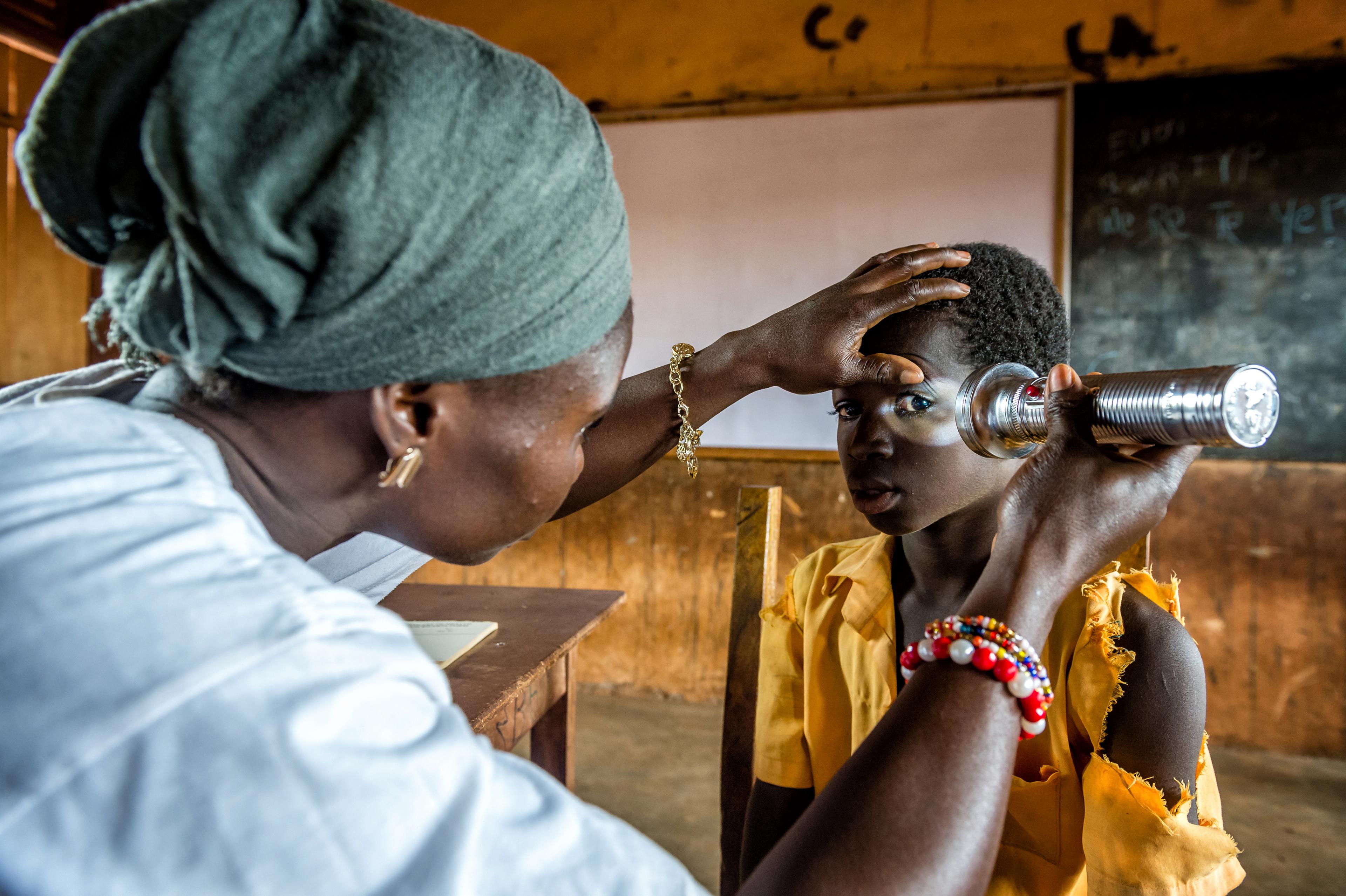 Mädchen bei einem Augentest in einer Schule bei Tamale. Eine Ärztin schaut ihr mit einer Taschenlampe ins linke Auge.