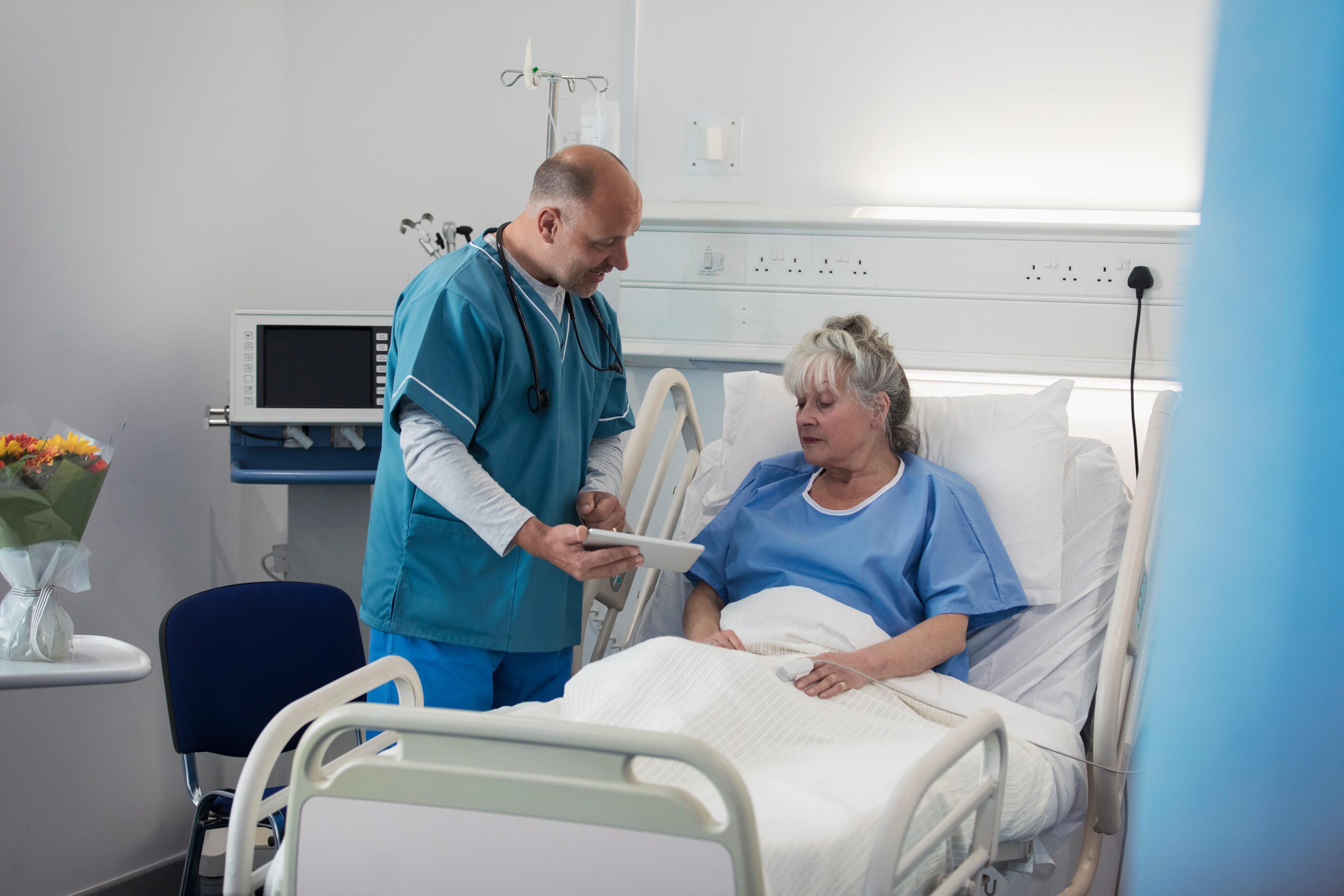 Un médecin dans une chambre d'hôpital montre des documents à une patiente allongée sur son lit.