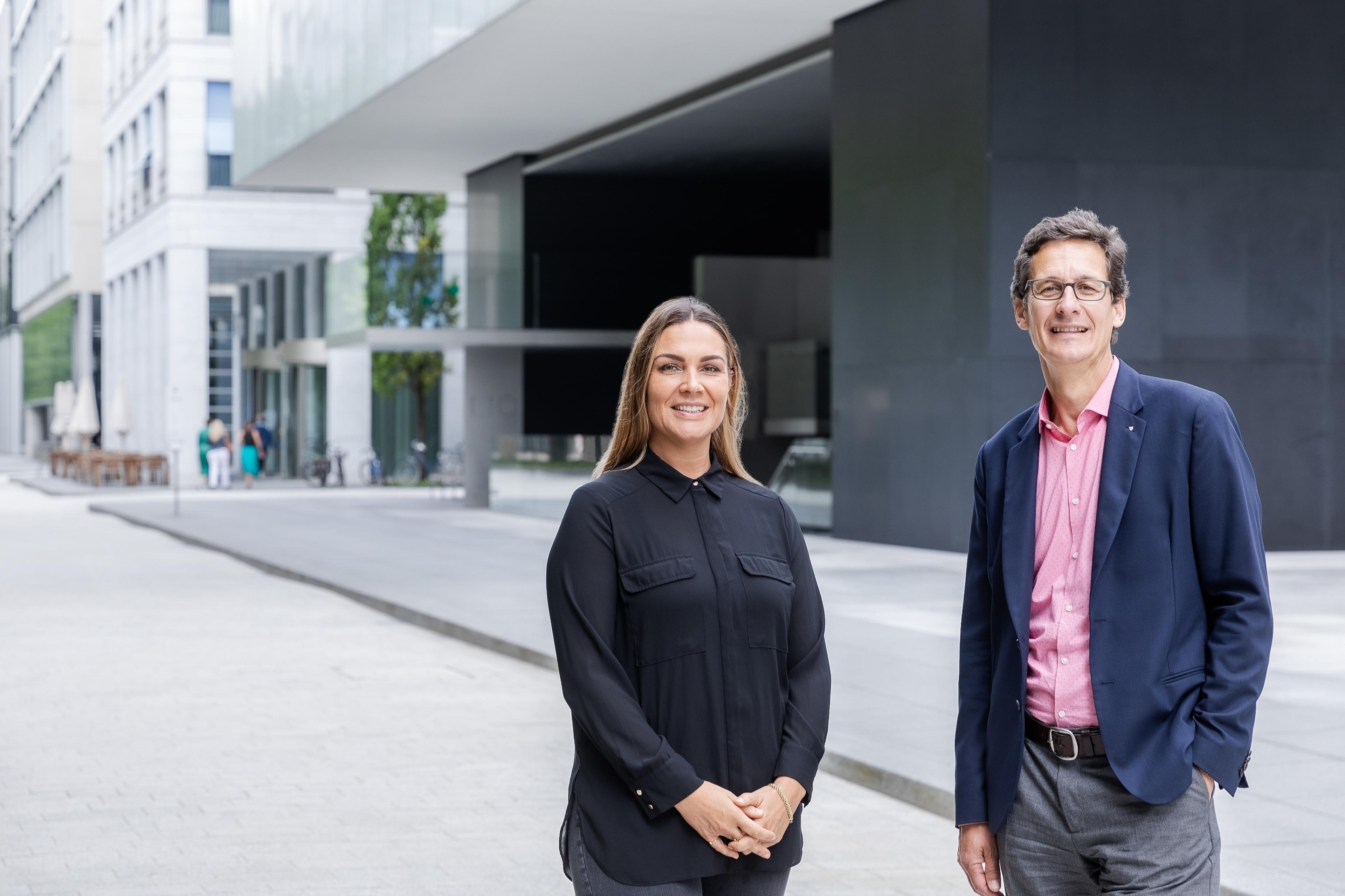 Isabel Dalli, Global Head Sponsoring & Donations di Novartis e Markus Mader, Direttore della Croce Rossa Svizzera, si trovano di fronte a un edificio moderno e sorridono alla telecamera.