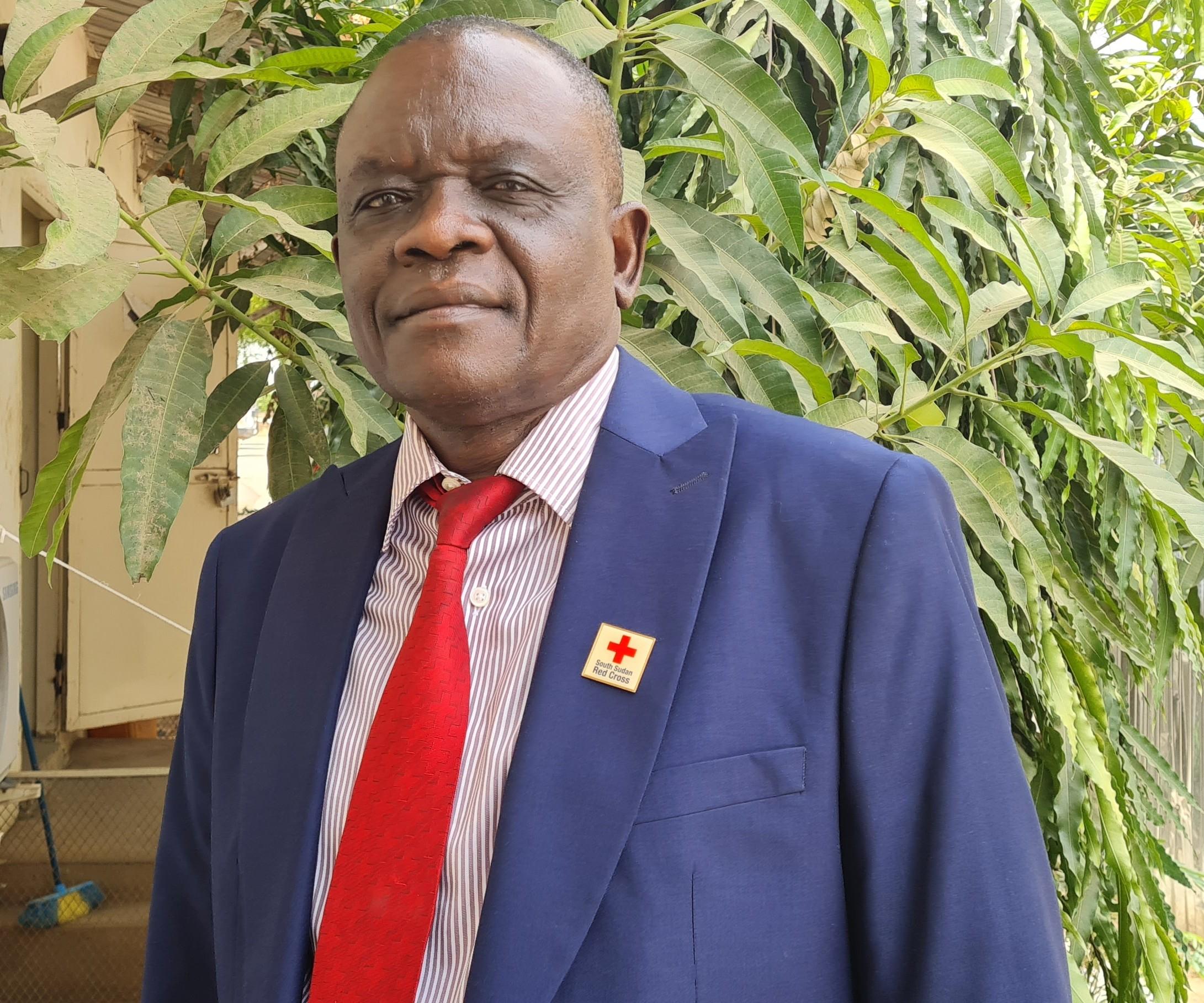 Photo portrait de John Lobor. Il porte un costume bleu avec une cravate rouge et un badge de la Croix-Rouge sud-soudanaise.