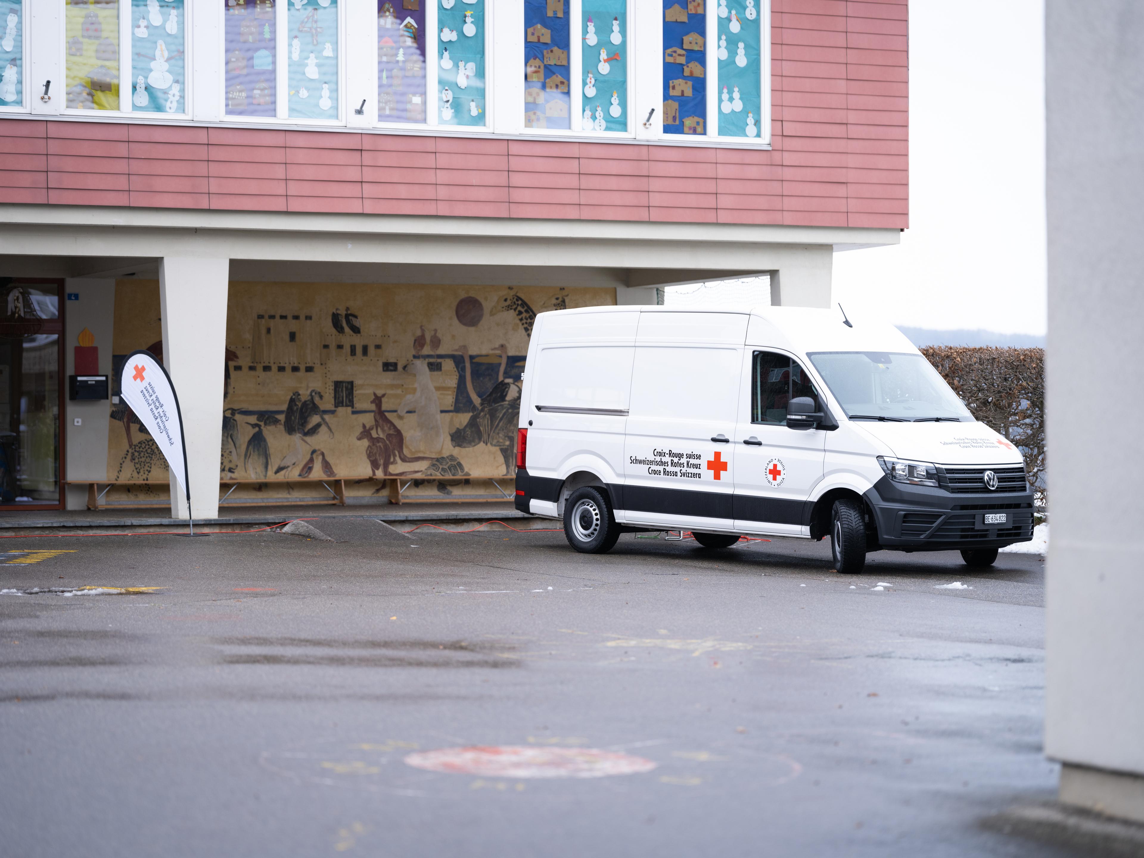 Un bus de la Croix-Rouge suisse est posté devant un bâtiment recouvert de dessins d'enfants.