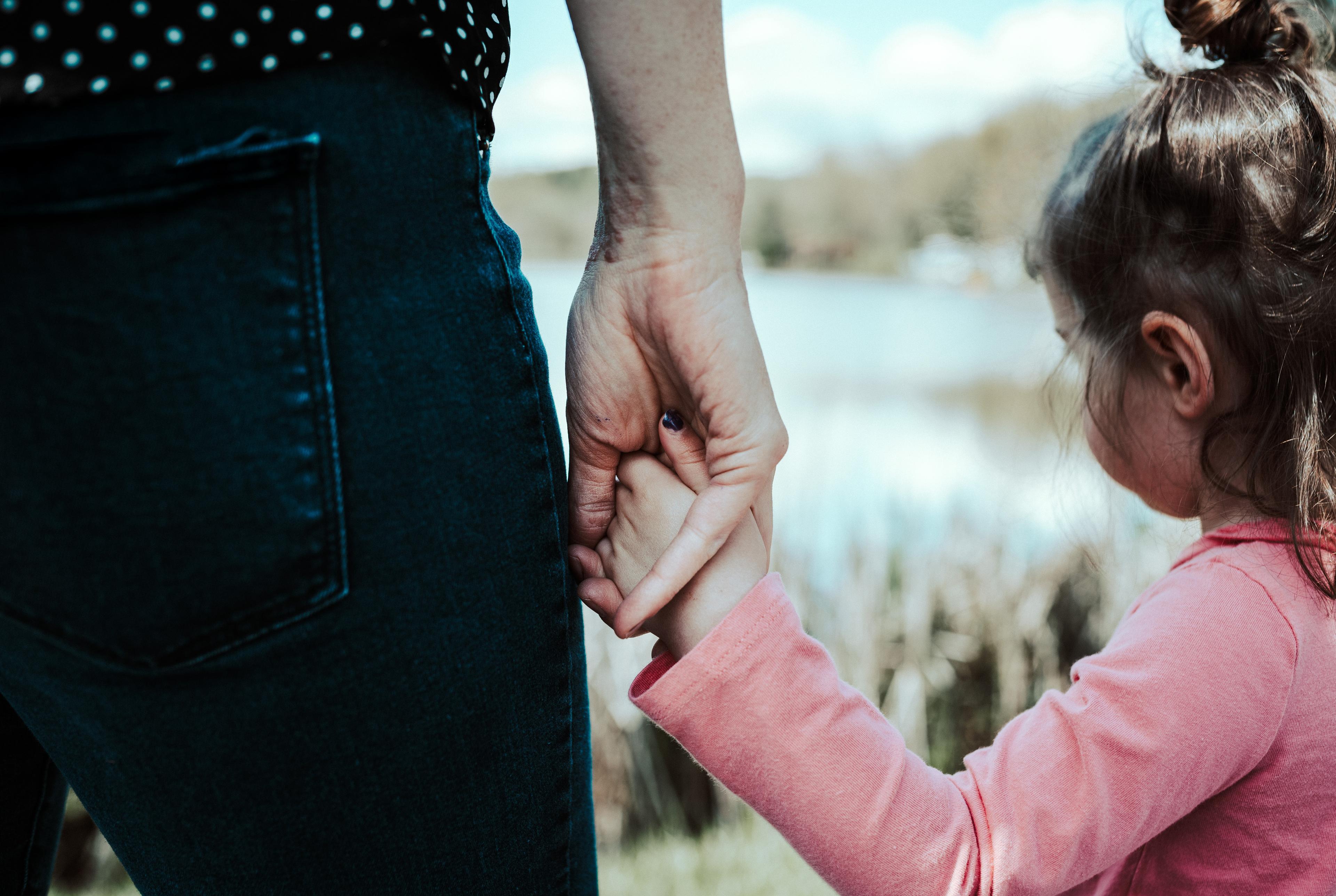 Immagine di una bambina di spalle che stringe la mano alla madre.