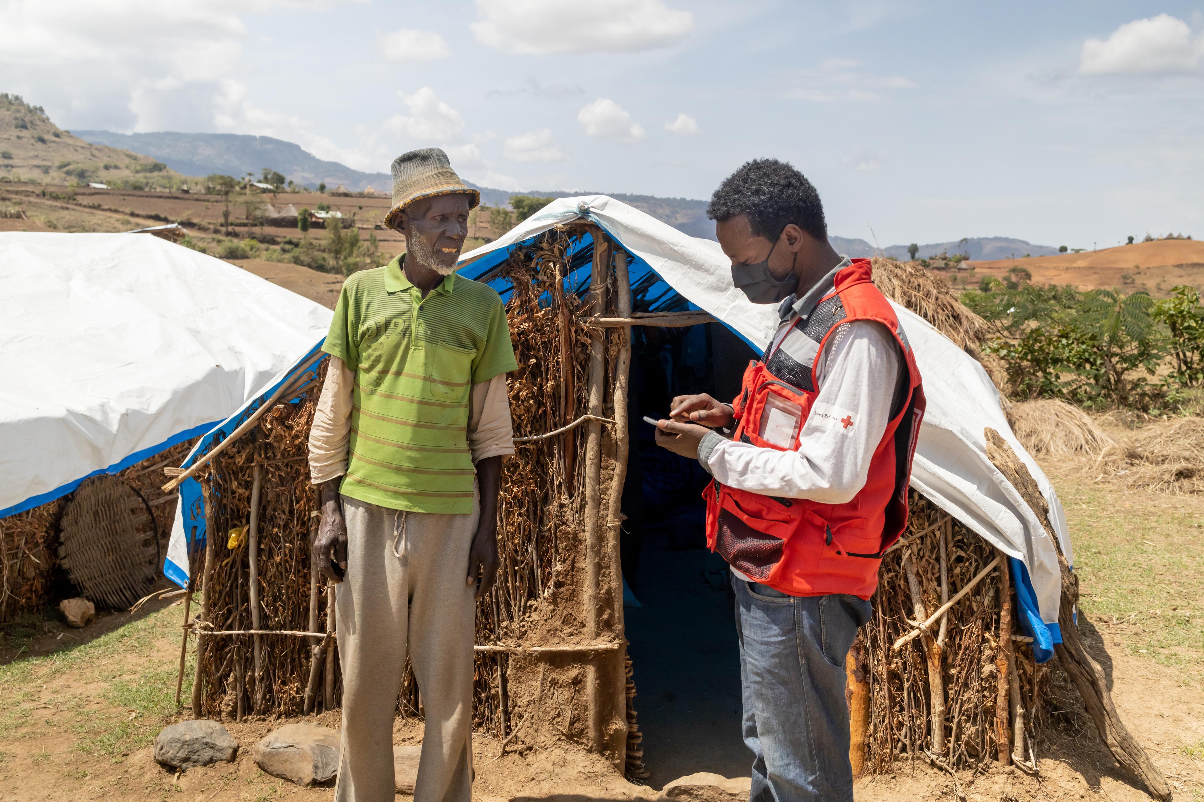 A man in front of a hut is questioned by a Red Cross worker.