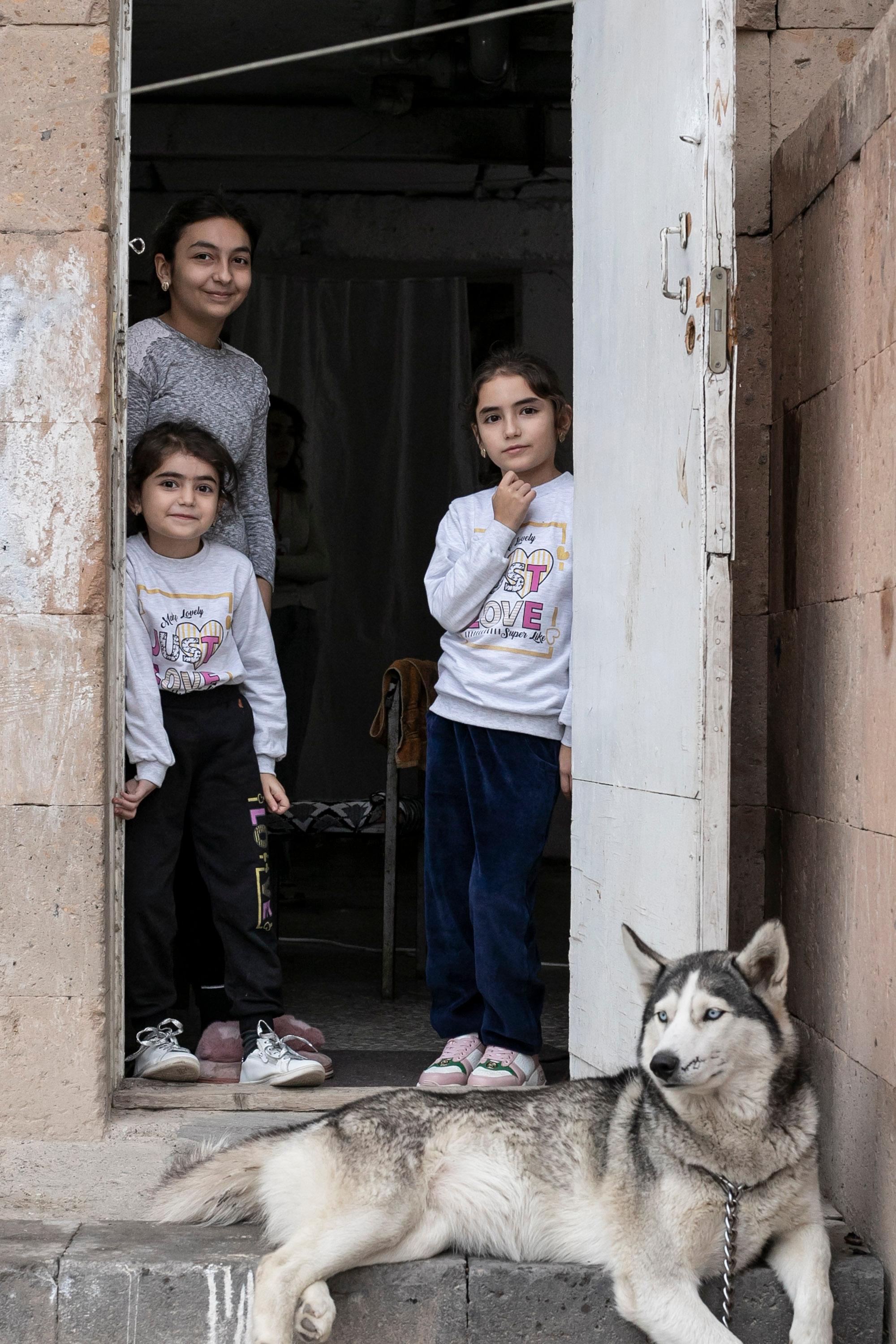 Drei Kinder schauen aus einer Türe. Ein Hund ist im Türrahmen zu sehen.