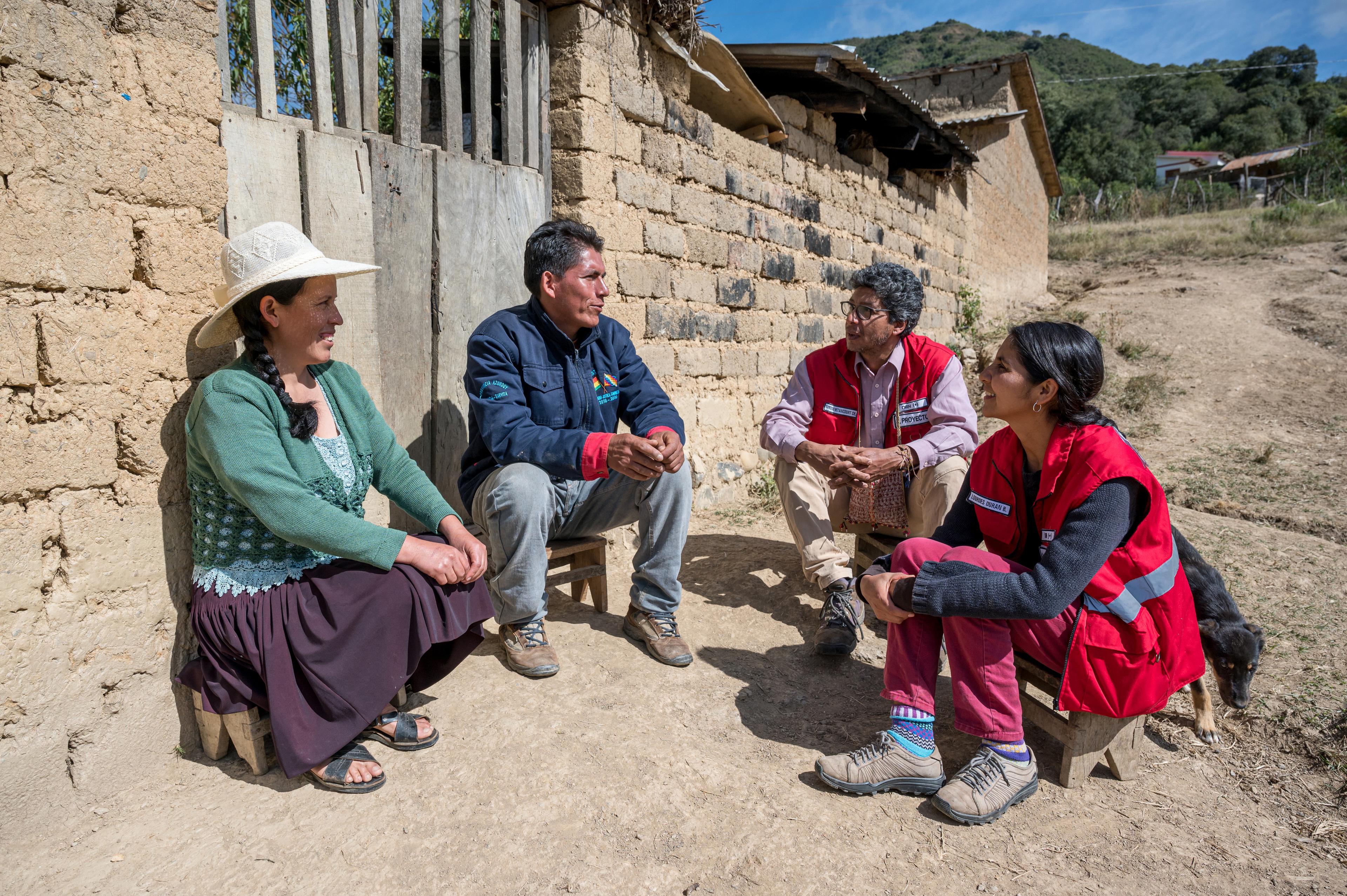 Quatre membres de la délégation de la CRS à Sucre, en Bolivie, sont assis en demi-cercle devant une maison, sur de petites banquettes, et discutent.