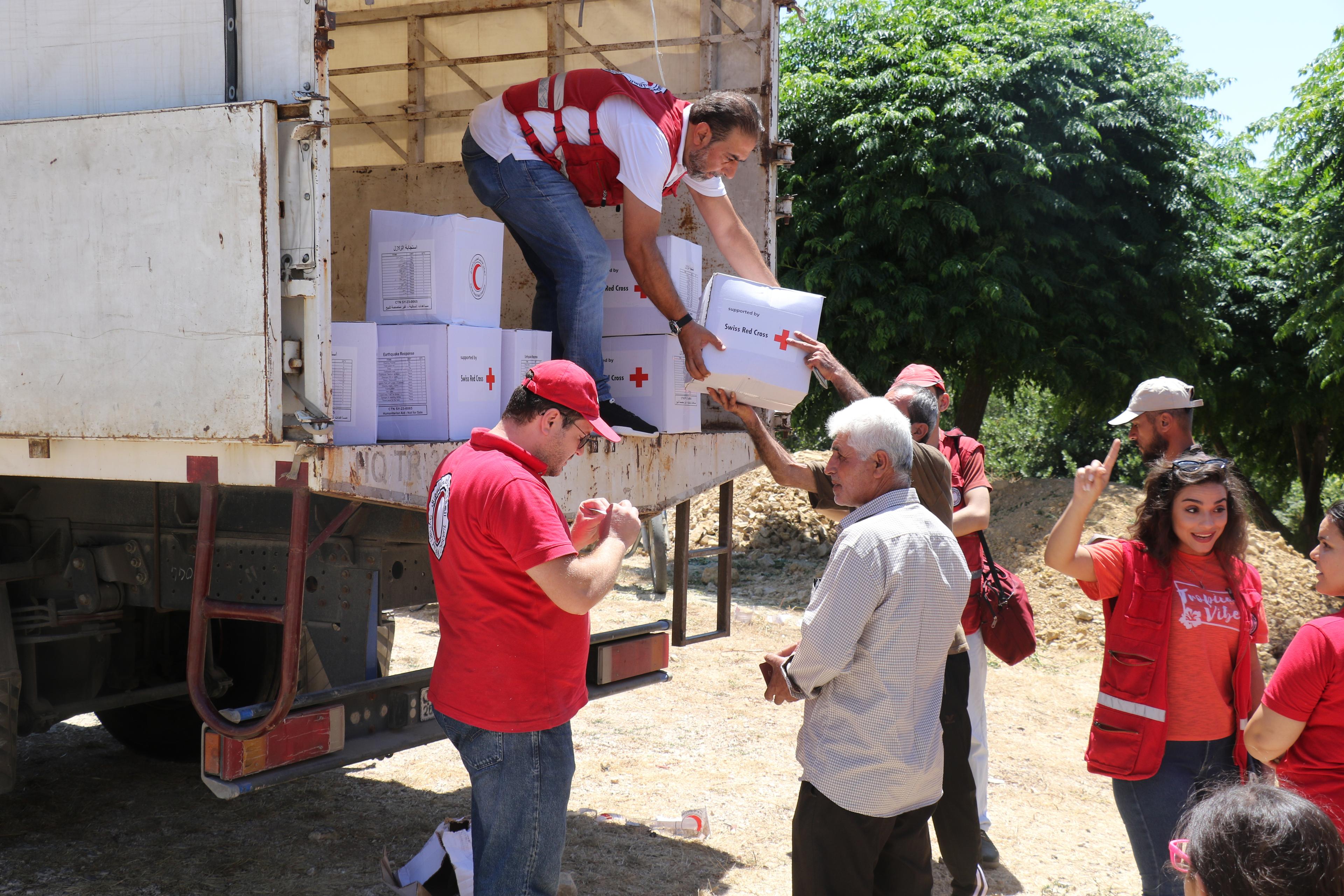 Du personnel du Croissant-Rouge arabe syrien décharge des cartons d'aide d'urgence. Sur les cartons figure le logo de la Croix-Rouge suisse