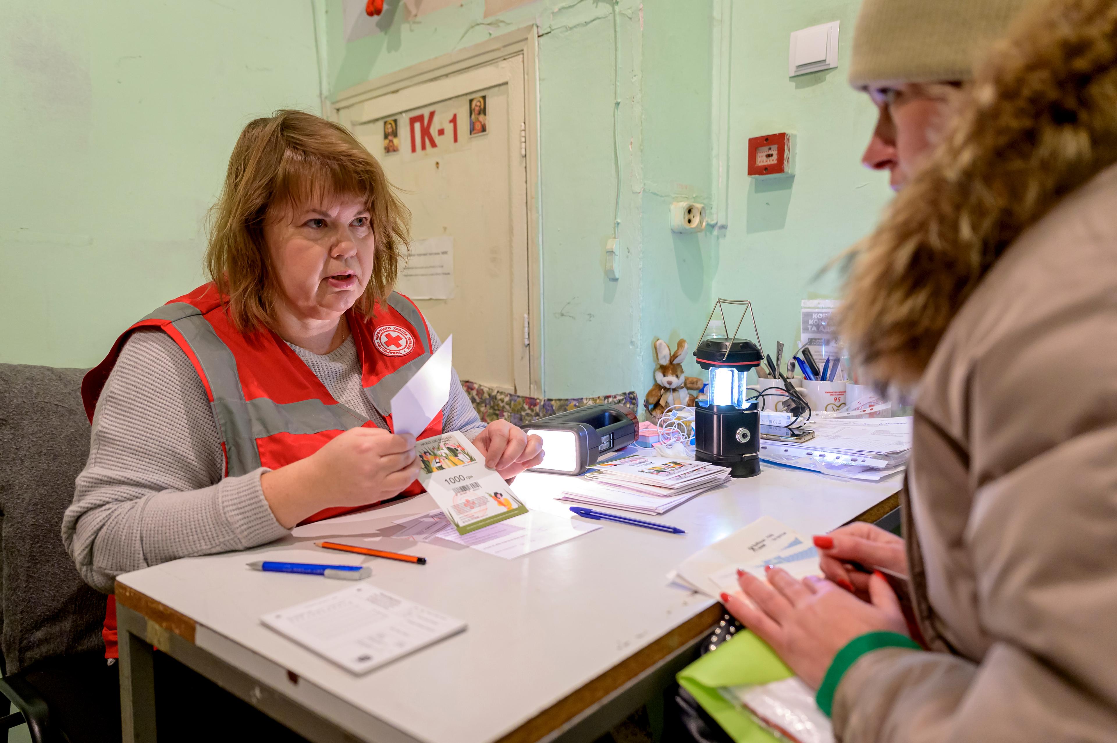 Un operatore della Croce Rossa si siede a un tavolo e consegna un buono a una donna.