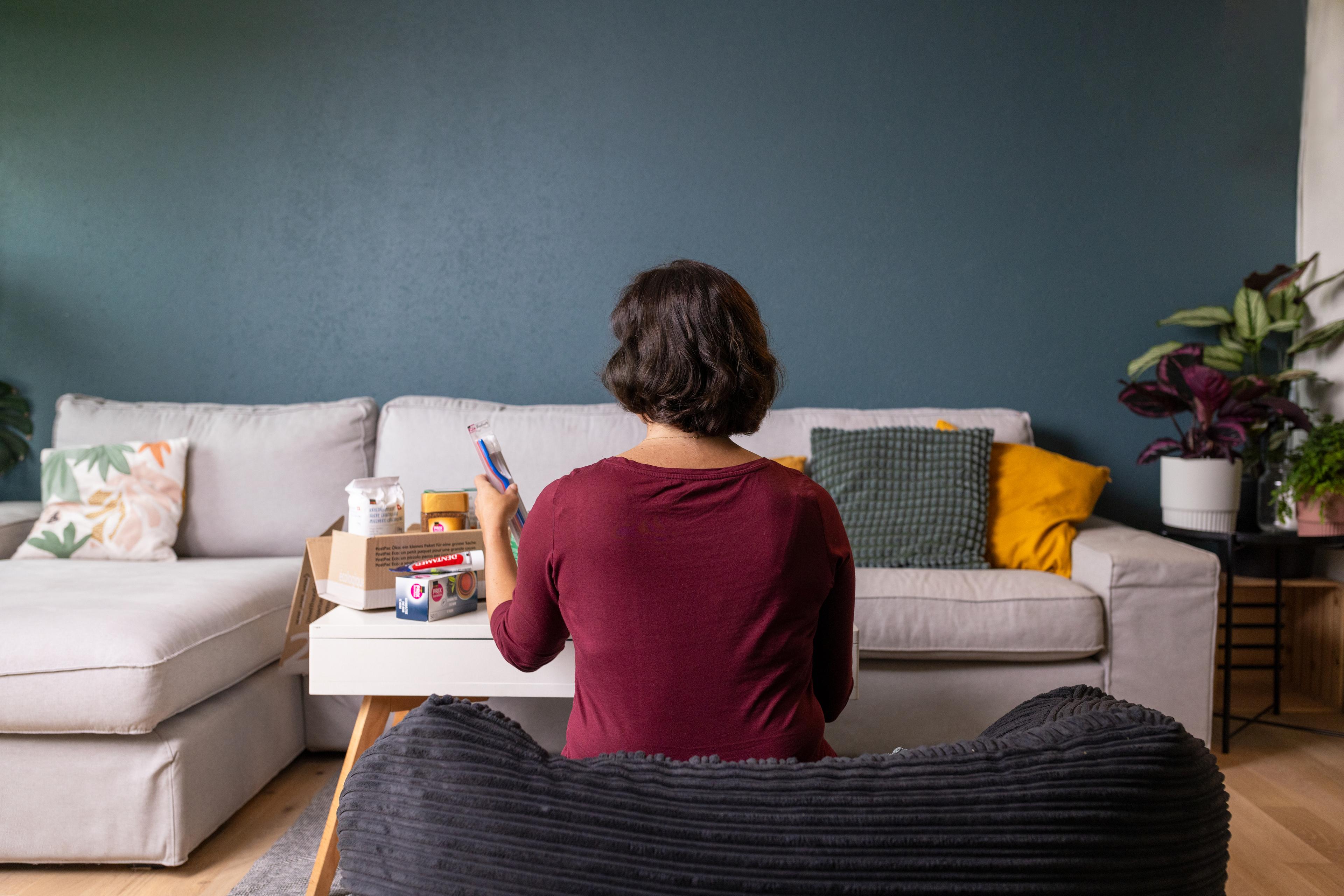 Una donna è seduta in soggiorno e disimballa prodotti per l'igiene e la spesa.