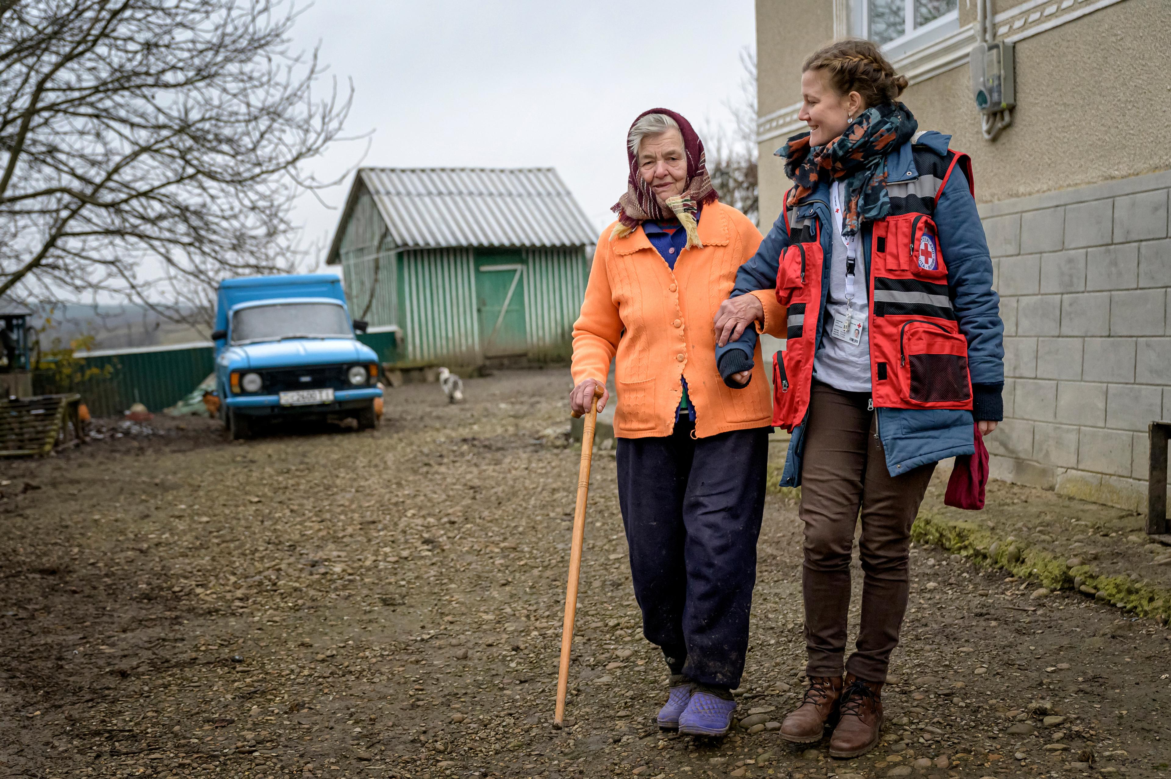 Une déléguée de la Croix-Rouge suisse donne le bras à une dame âgée devant une maison de Ternopil en Ukraine.