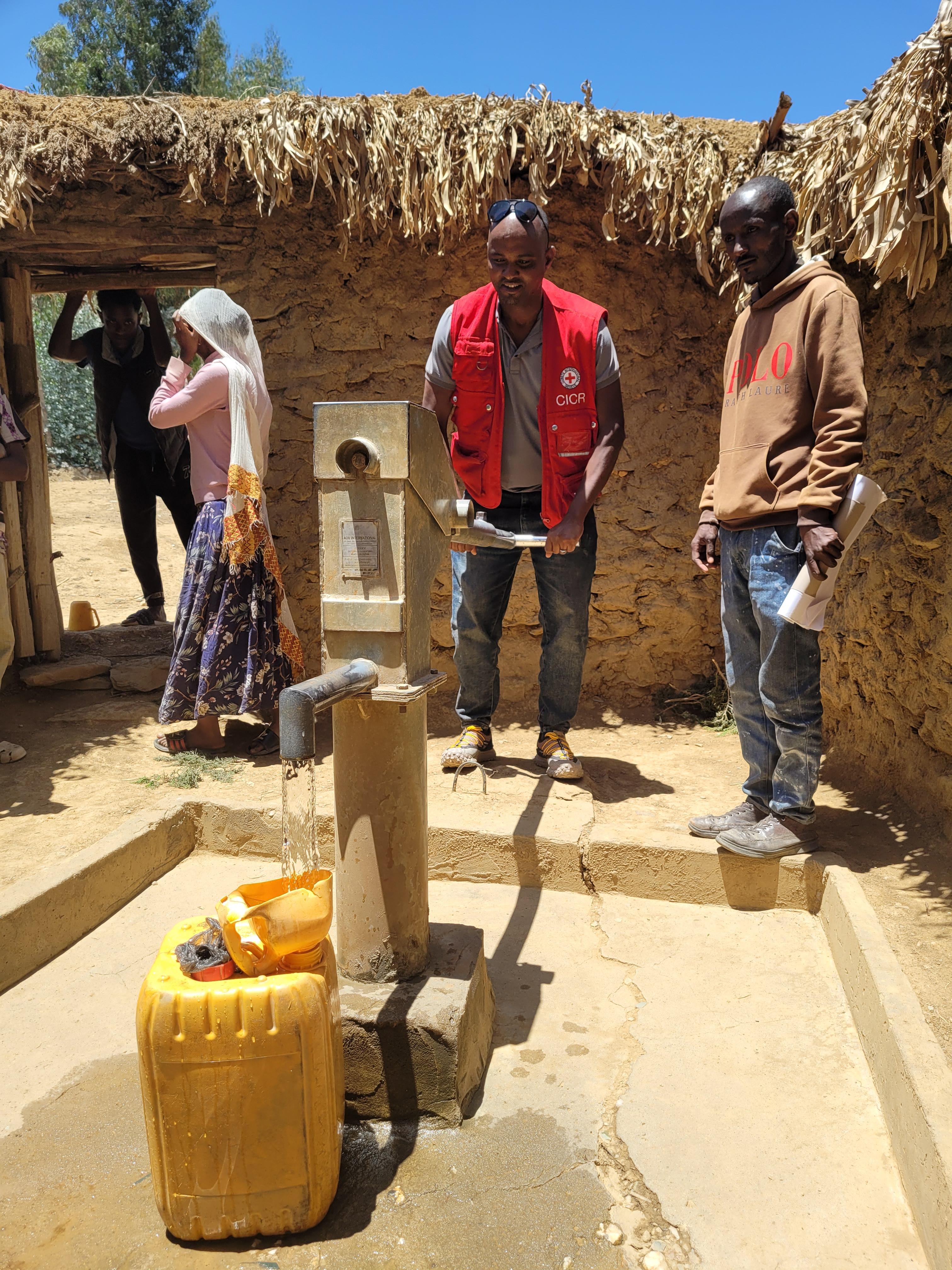 Mitarbeitende des Roten Kreuzes testen eine Wasser-Handpumpe.
