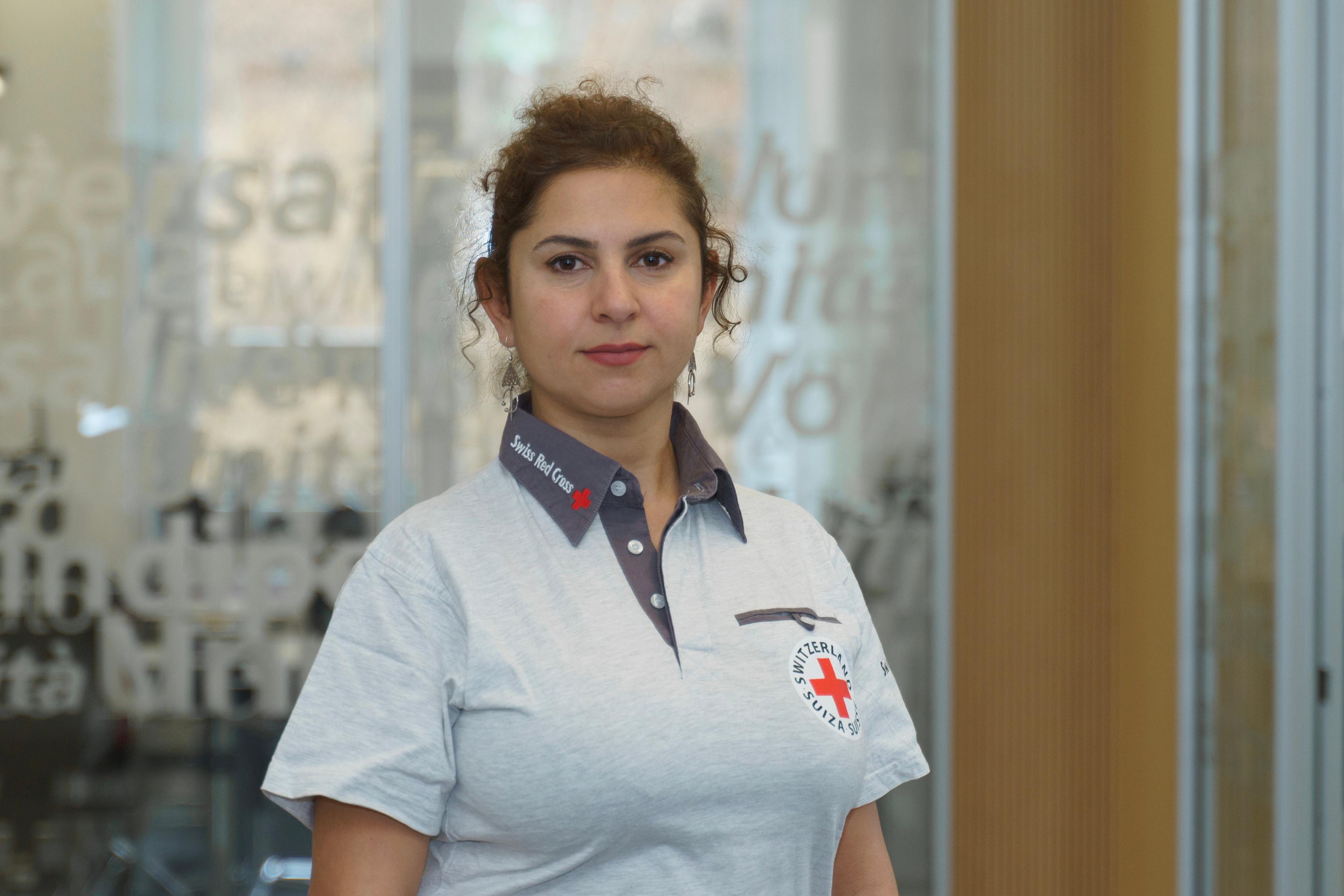 Eine Frau mit zusammen gebunden braun-rötlichen Haaren blickt direkt in die Kamera. Sie trägt ein graues Polo-Shirt mit der Aufschrift Swiss Red Cross. 