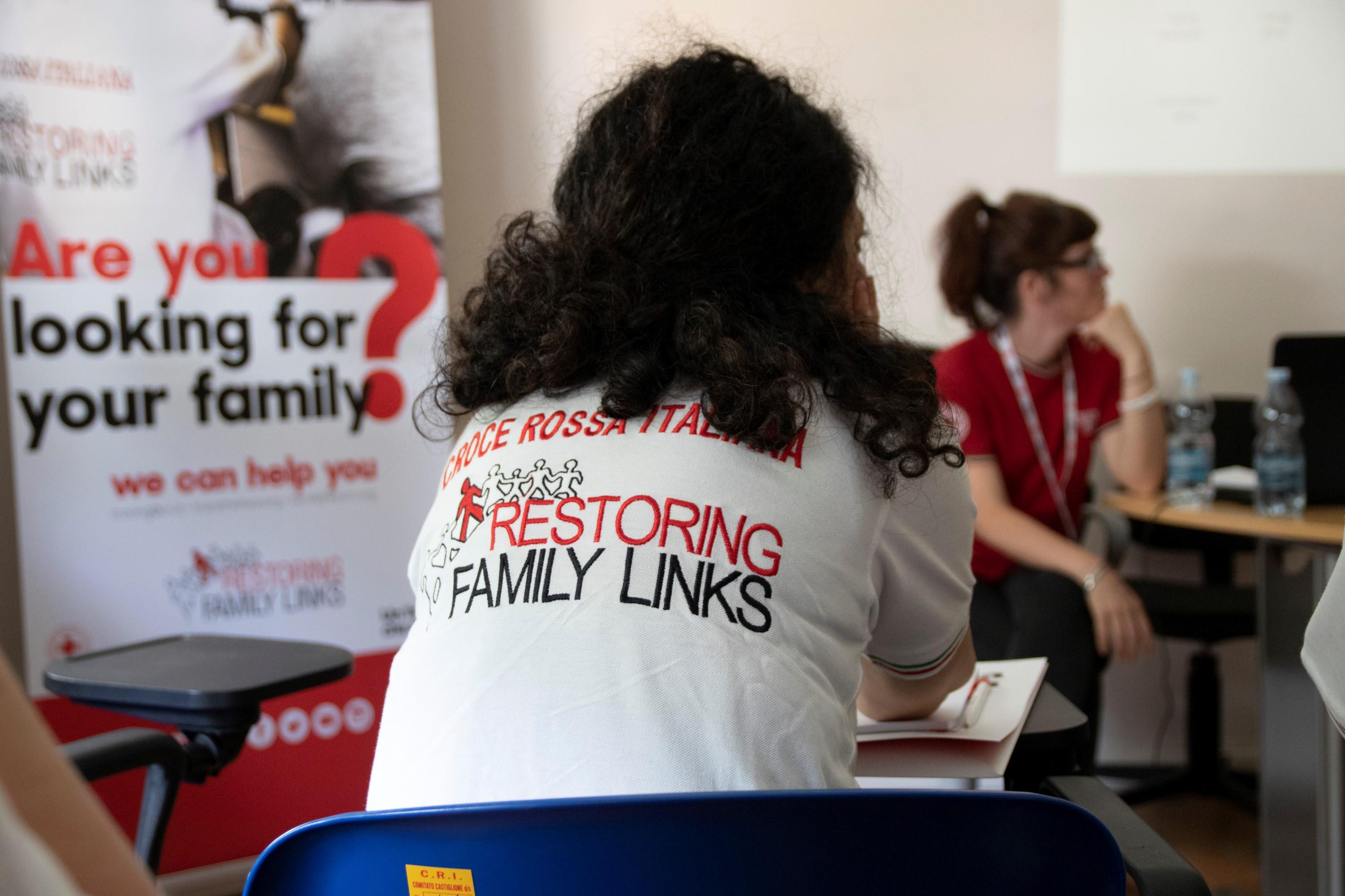 Vue de dos d'une collaboratrice de la Croix-Rouge italienne. Sur sa chemise figure le logo du réseau "Restoring Family Links".