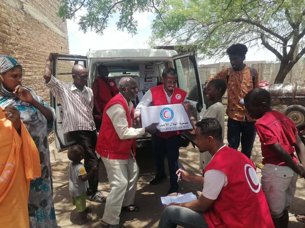 Trois volontaires du Croissant-Rouge soudanais en veste rouge apportent déchargent des paquets d'aide alimentaires pour la population.